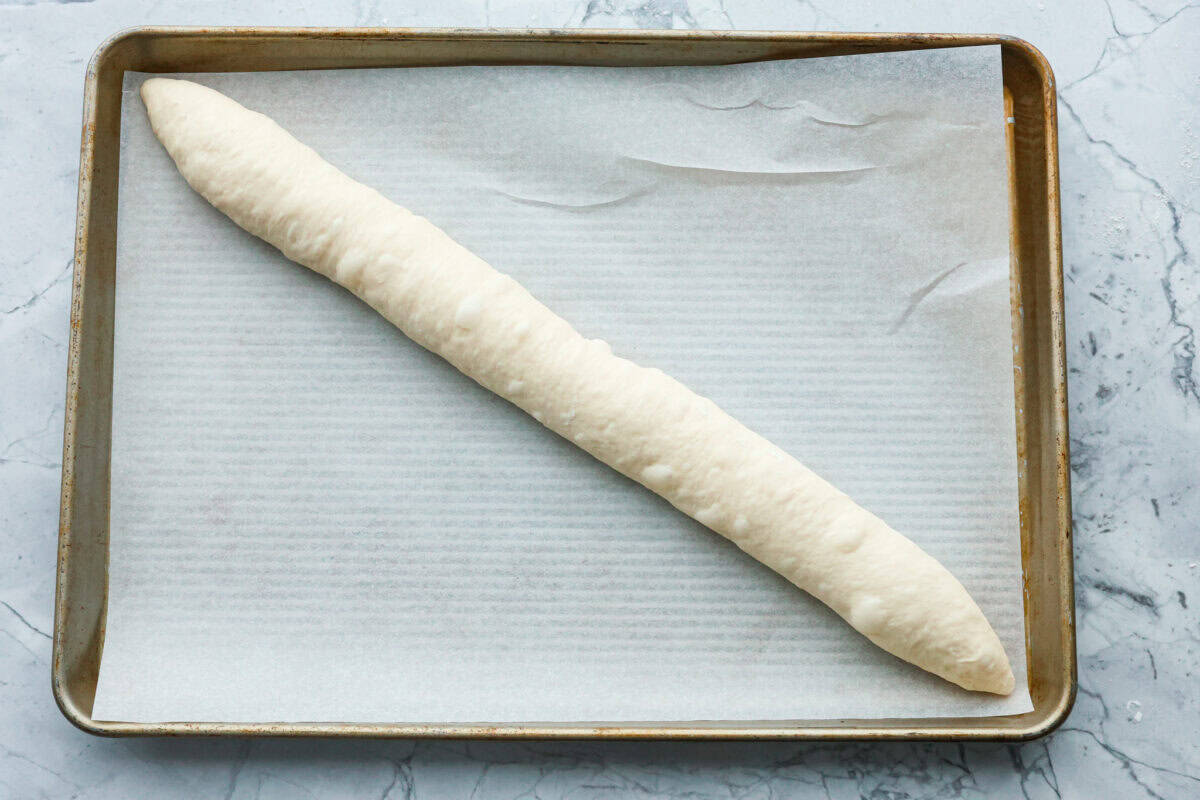 This French baguette recipe is super easy and will change your life! It has a perfect crusty outside and tender, soft inside, perfect for your bread cravings. Overhead shot of French baguette dough at an angle on a parchment lined baking sheet.