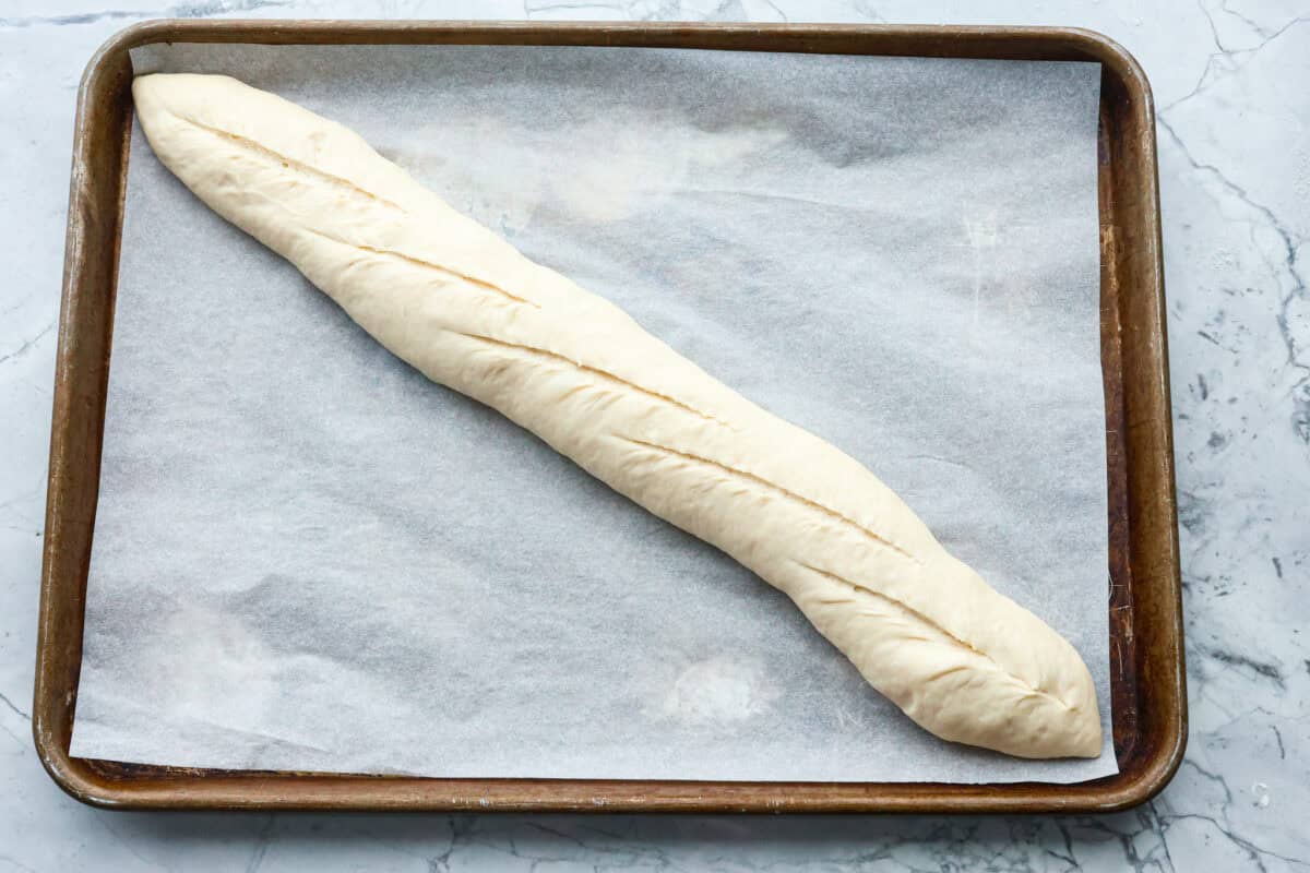 This French baguette recipe is super easy and will change your life! It has a perfect crusty outside and tender, soft inside, perfect for your bread cravings. Overhead shot of dough loaf with score marks across the top.