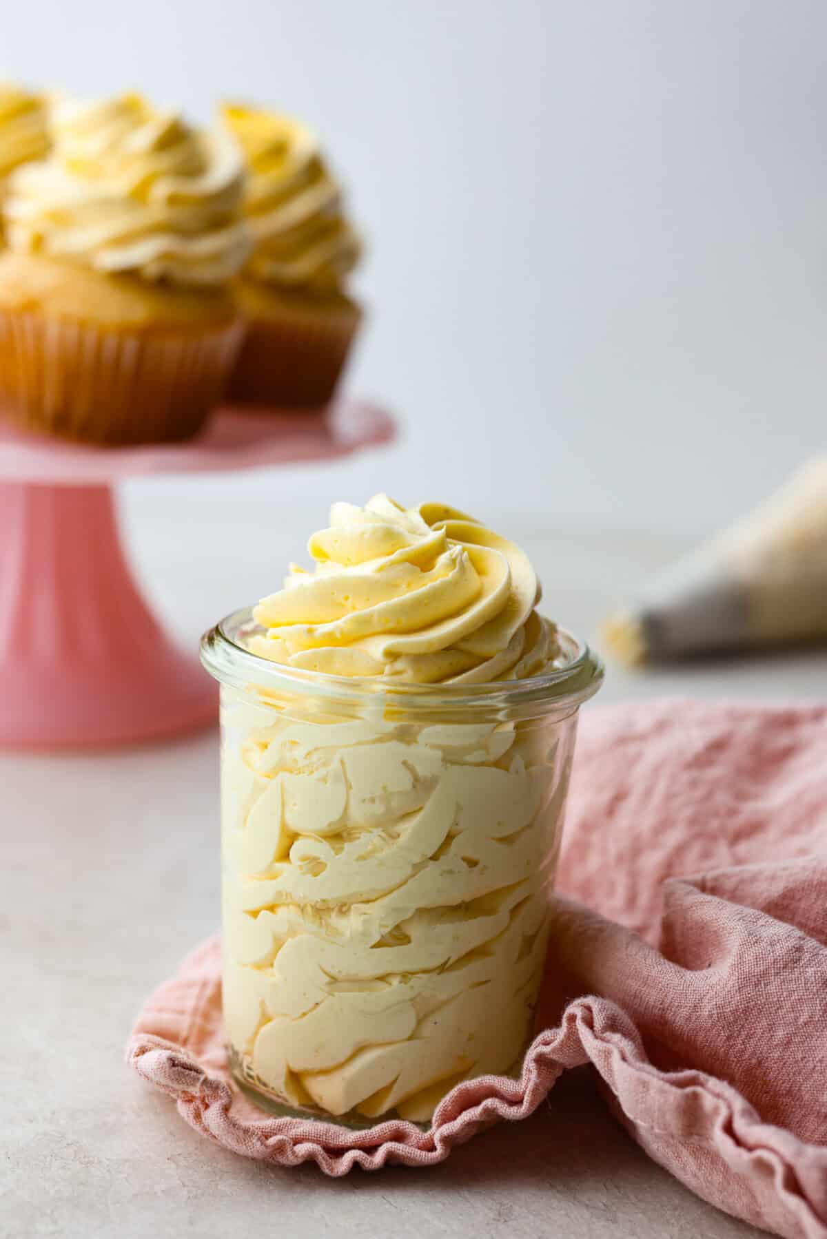 French buttercream is a luxurious, creamy frosting that will wow your guests and tantalize your taste buds. The elegant flavor comes from using egg yolks as the base and delicious, simple syrup for sweetness. Elevate your baking game with this unique recipe. Side shot of french buttercream piped into a small glass jar.