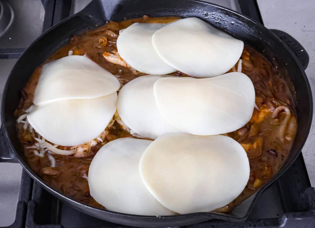 Skillet French Onion Chicken delivers a tender and creamy chicken dinner that you can make at home, it's easily better than anything you can find in a restaurant. Your family will love this incredibly delicious meal, making it an instant favorite! Overhead shot of cheese on top of chicken breasts in skillet completing the French onion chicken.