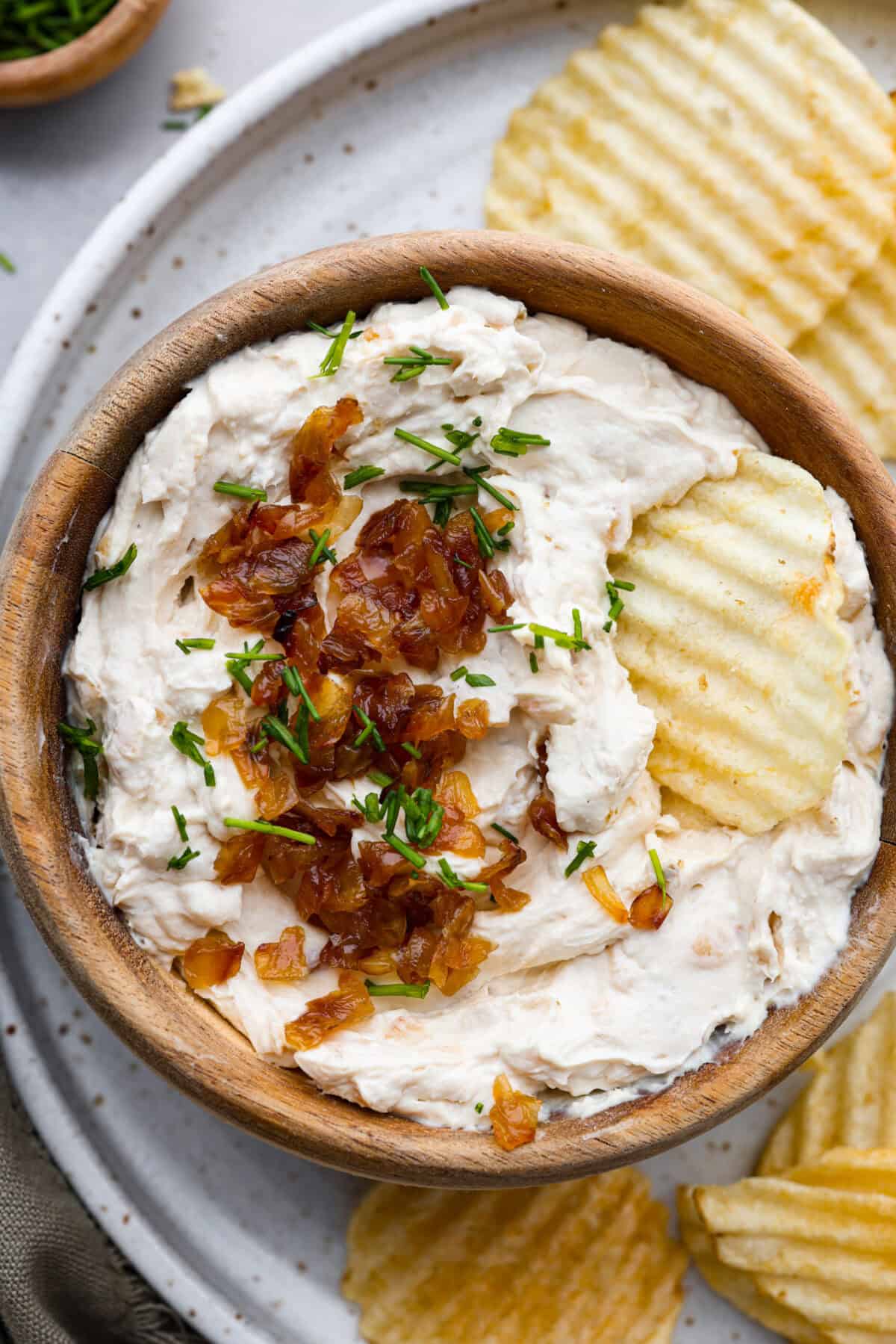 The Best French Onion Dip begins with caramelized onions that combine with cream cheese, sour cream, and seasonings. It creates a dip so addictive and creamy, it'll be gone before you know it! Top view of French onion dip garnished with caramelized onions and a chip on top.
