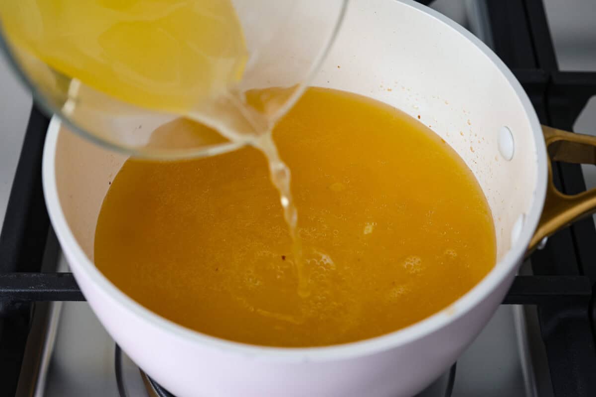 Garlic Butter Rice is the perfect side dish for dinner! A simpleย mix of butter, sautรฉed onion, garlic, and chicken brothย gives this rice tons of great flavor. It's easy to make and tastes amazing! Overhead shot of someone pouring chicken broth into the onion, butter and garlic mixture.