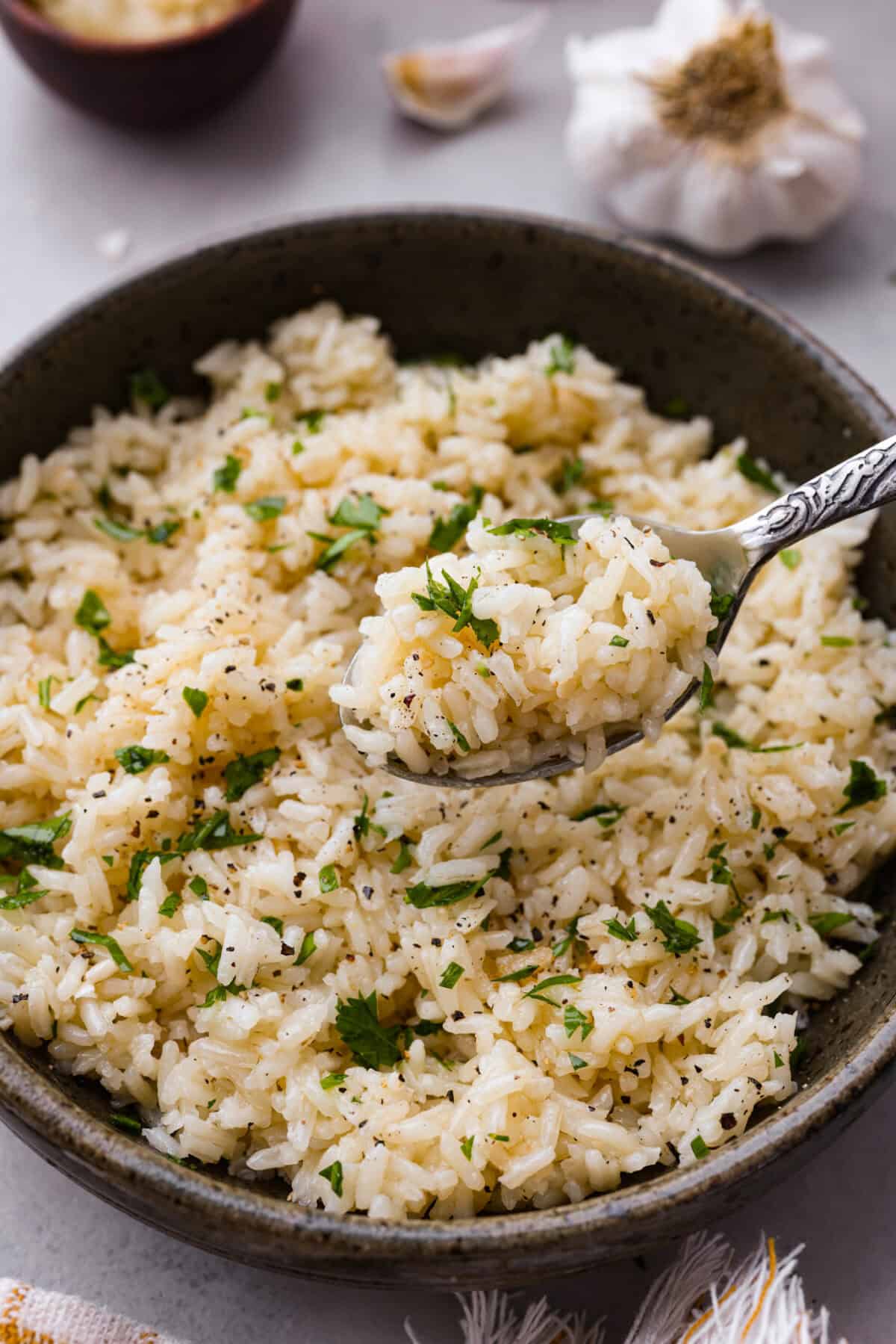 Garlic Butter Rice is the perfect side dish for dinner! A simpleย mix of butter, sautรฉed onion, garlic, and chicken brothย gives this rice tons of great flavor. It's easy to make and tastes amazing! Angle shot of a plated bowl of garlic butter rice with a bite of rice on a spoon.