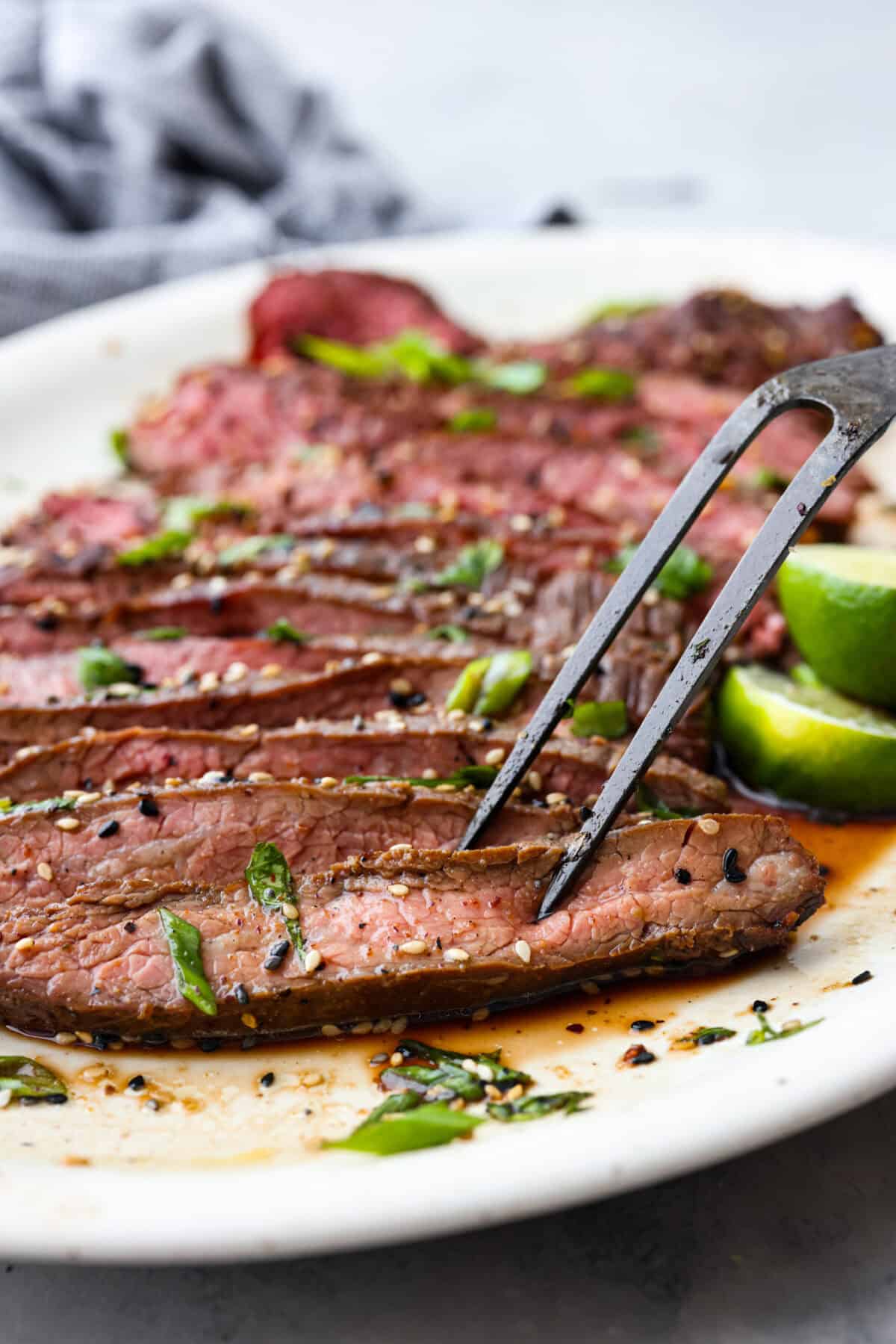 This grilled flank steak with Asian-inspired marinade features a savory blend of soy sauce, ginger, and garlic. The steak is seared to perfection on a hot grill, locking in all the delicious flavors. Best of all, itโs ready in less than 10 minutes! Close up shot of large fork skewering slice of steak.