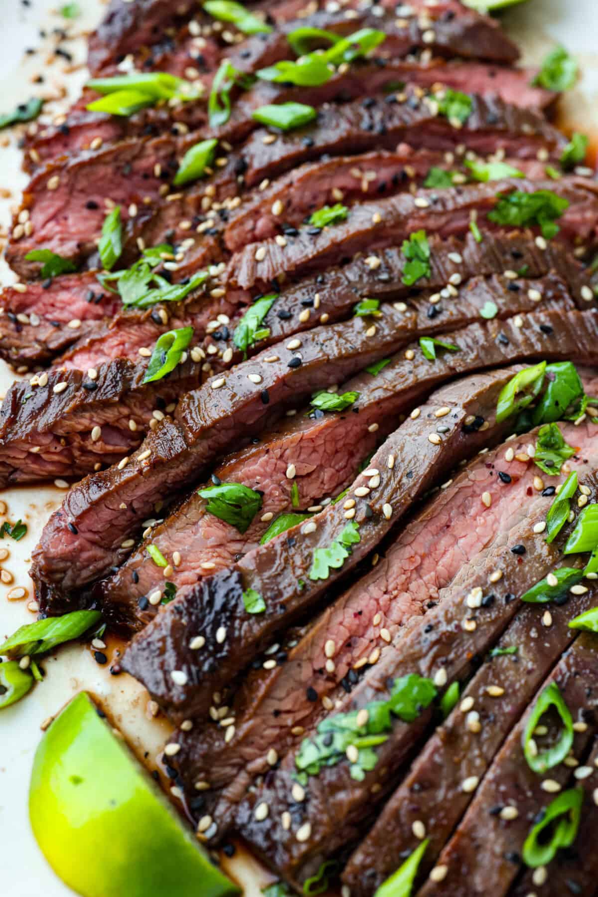This grilled flank steak with Asian-inspired marinade features a savory blend of soy sauce, ginger, and garlic. The steak is seared to perfection on a hot grill, locking in all the delicious flavors. Best of all, itโs ready in less than 10 minutes! close up shot of sliced steak.
