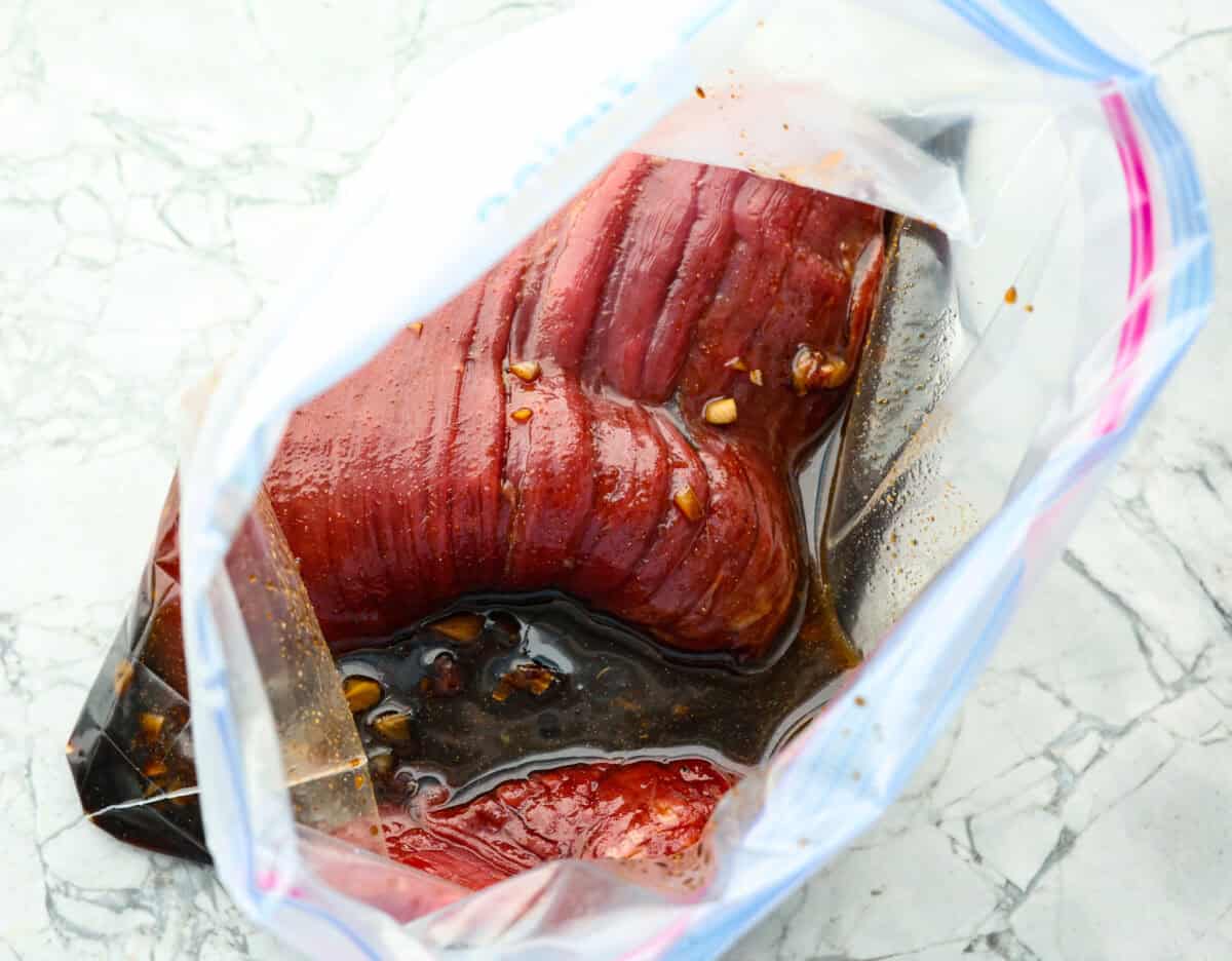 This grilled flank steak with Asian-inspired marinade features a savory blend of soy sauce, ginger, and garlic. The steak is seared to perfection on a hot grill, locking in all the delicious flavors. Best of all, itโs ready in less than 10 minutes! Overhead shot of flank steak in larg zip-lock bag with marinade.