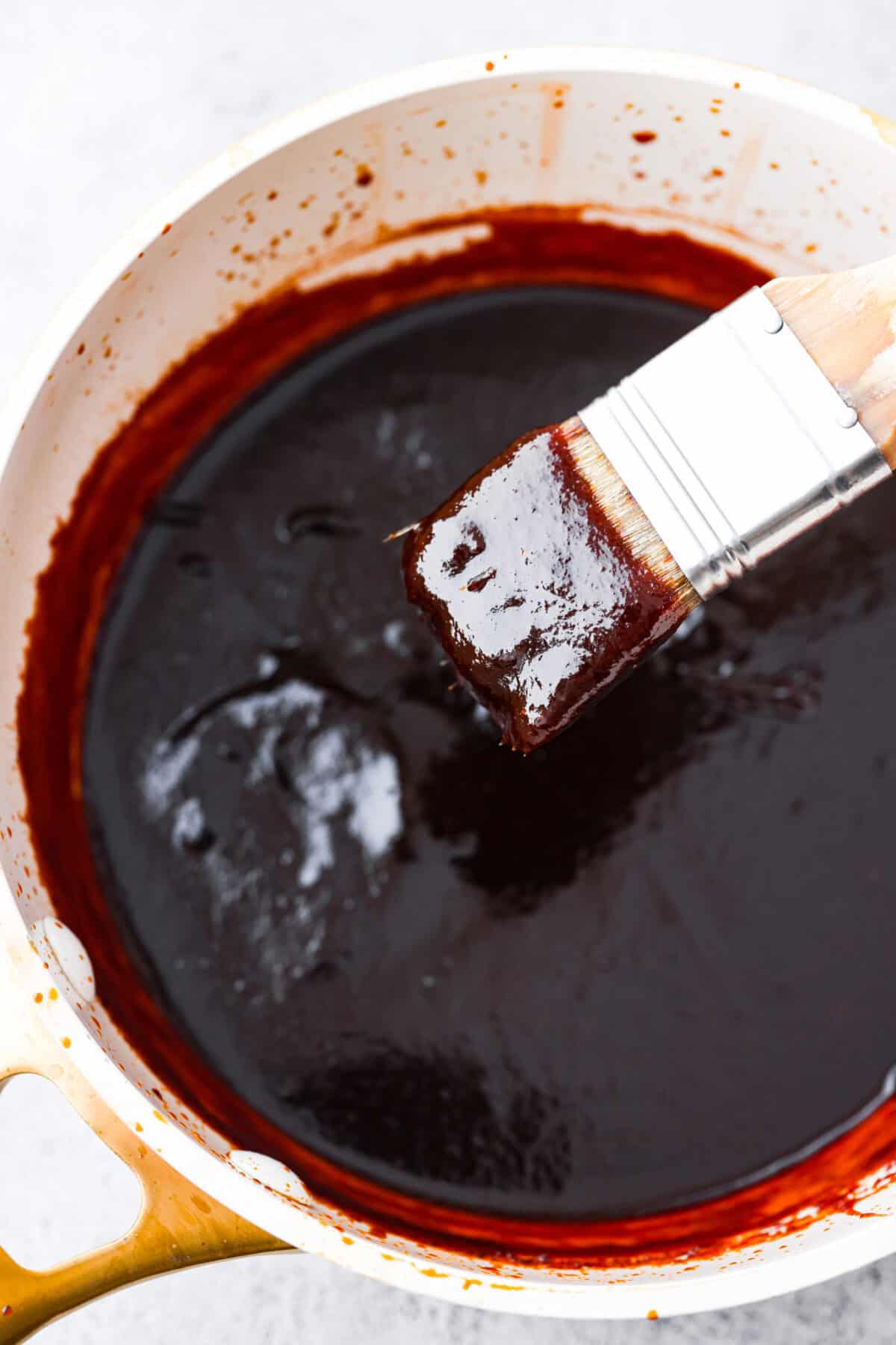 This Homemade BBQ Sauce recipe has the most amazing flavor combination and only takes minutes to make! It's sweet and tangy and has the perfect amount of smokiness that makes this BBQ sauce a family favorite! Top view of bbq sauce in a saucepan with a basting brush.