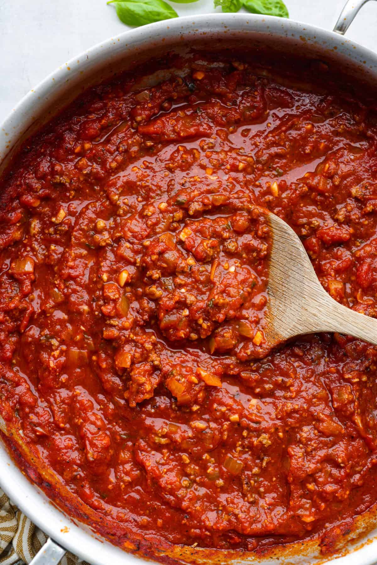 There's no need to purchase store-bought sauce, with this hearty and flavorful Homemade Spaghetti Sauce. Simple ingredients such as ground beef, onion, garlic, and spices of oregano and basil bring a bold flavor to this simple sauce. Top close view of homemade spaghetti sauce in a silver pan with a wood spoon.