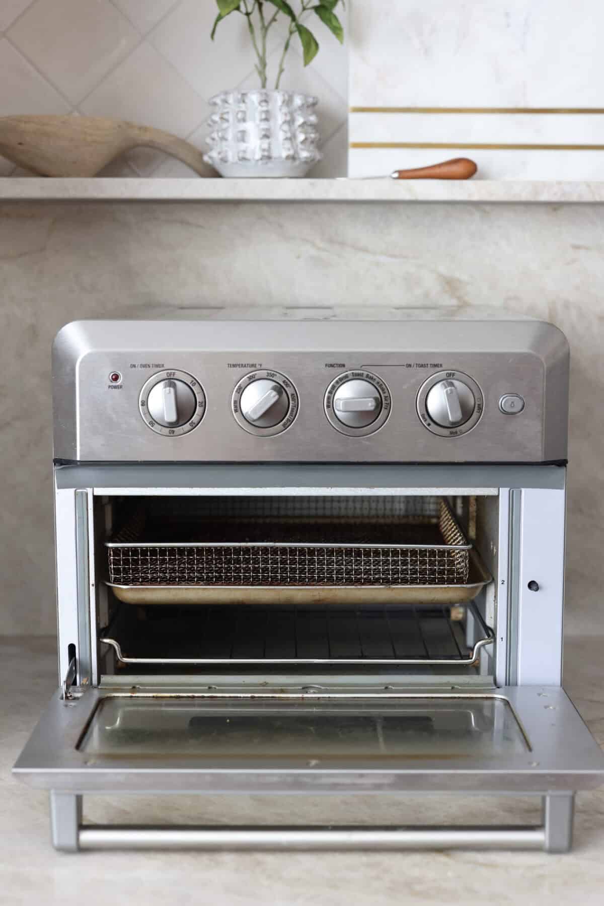 The air fryer is one of the most versatile appliances in today's kitchen! Learn how to use an air fryer to cook, reheat, and achieve that "fried" texture without frying in oil. Once you cook in the air fryer you will never look back! Close view of a toaster oven air fryer with the door open.