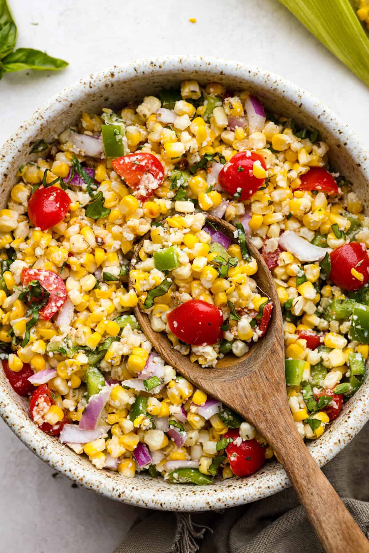 This Italian Corn Salad is bursting with fresh flavors from sweet corn, juicy grape tomatoes, crisp green bell pepper, and sharp parmesan cheese. Tossed in a zesty homemade Italian dressing, it’s perfect for summer or any time of the year. Overhead shot of Italian corn salad in bowl with wooden spoon.