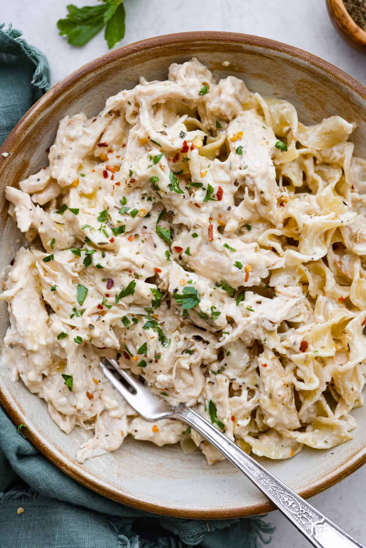 Italian cream cheese chicken is a simple way to enjoy tender, creamy, flavorful chicken over noodles, rice, or potatoes. With only four ingredients, this is definitely one of those slow cooker recipes you will have on repeat. Overhead shot of a bowl of Italian cream cheese chicken over egg noodles.