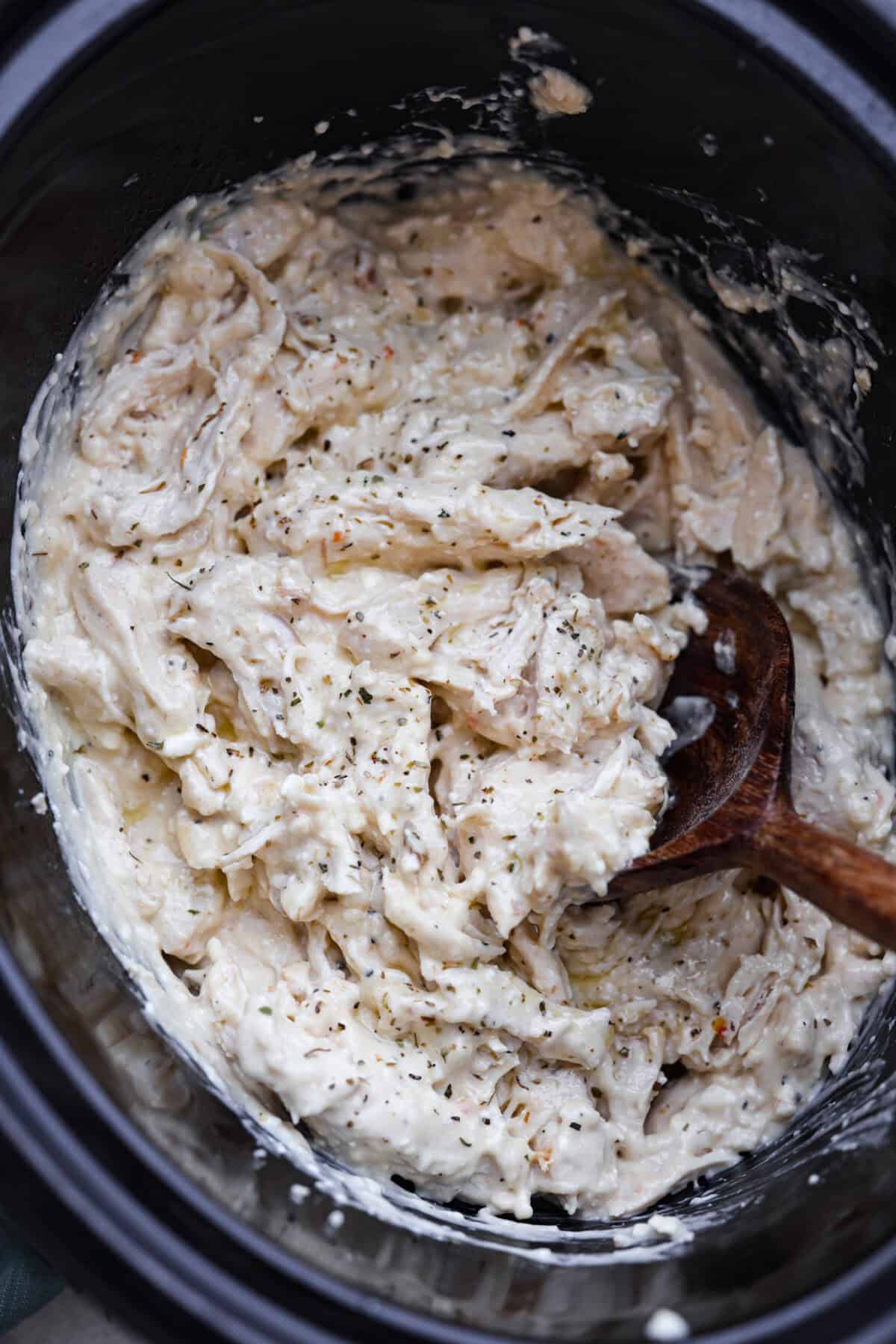 Italian cream cheese chicken is a simple way to enjoy tender, creamy, flavorful chicken over noodles, rice, or potatoes. With only four ingredients, this is definitely one of those slow cooker recipes you will have on repeat. Overhead shot of cooked Italian cream cheese chicken in crockpot with wooden spoon.