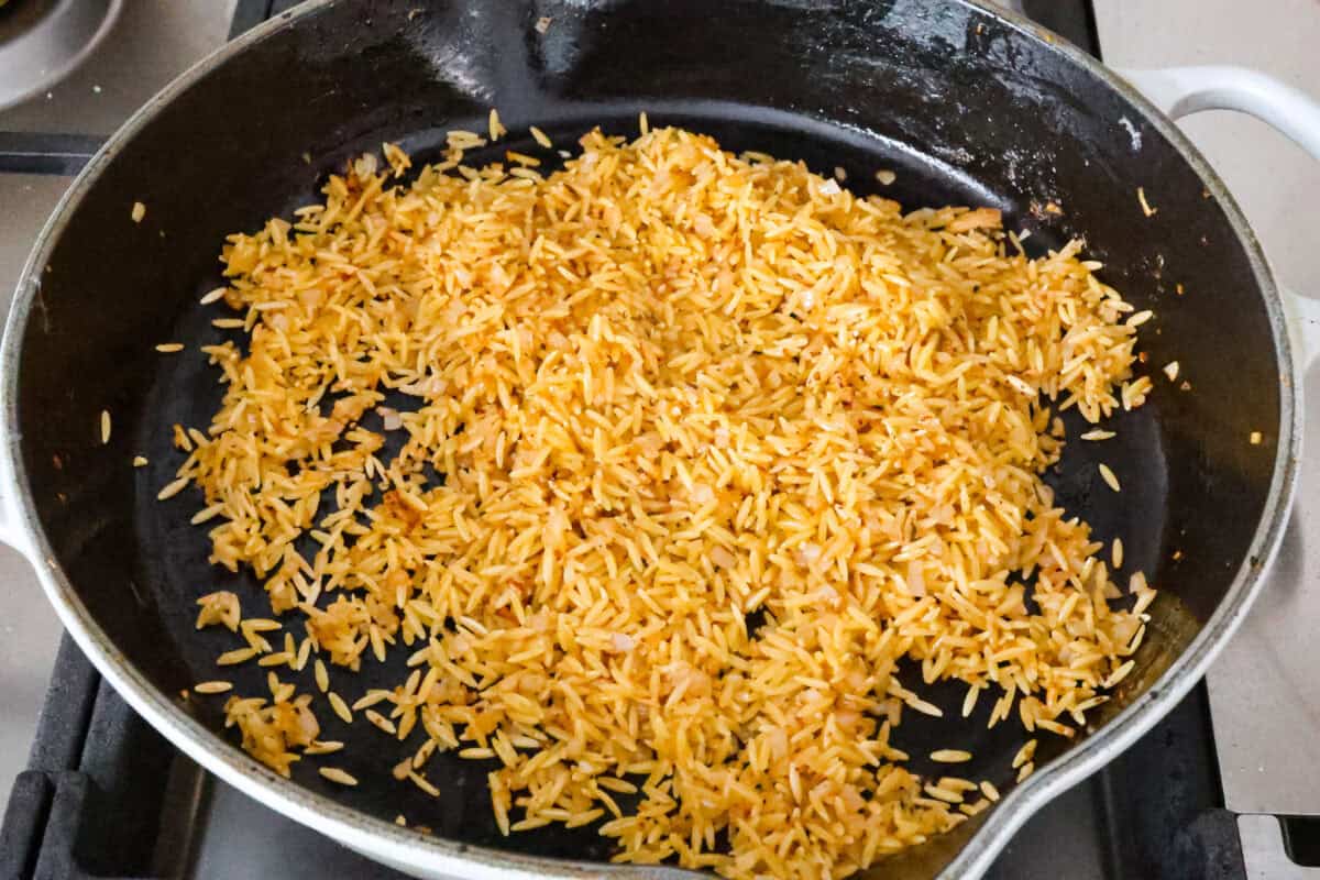 One-Pan Lemon Chicken Orzo is a comforting, well-rounded meal! Tender, juicy chicken pieces are joined with orzo pasta in a bright lemon sauce, resulting in melt-in-your-mouth deliciousness! Your whole family will adore this tasty dinner! Angle shot of orzo pasta being browned in a pan.
