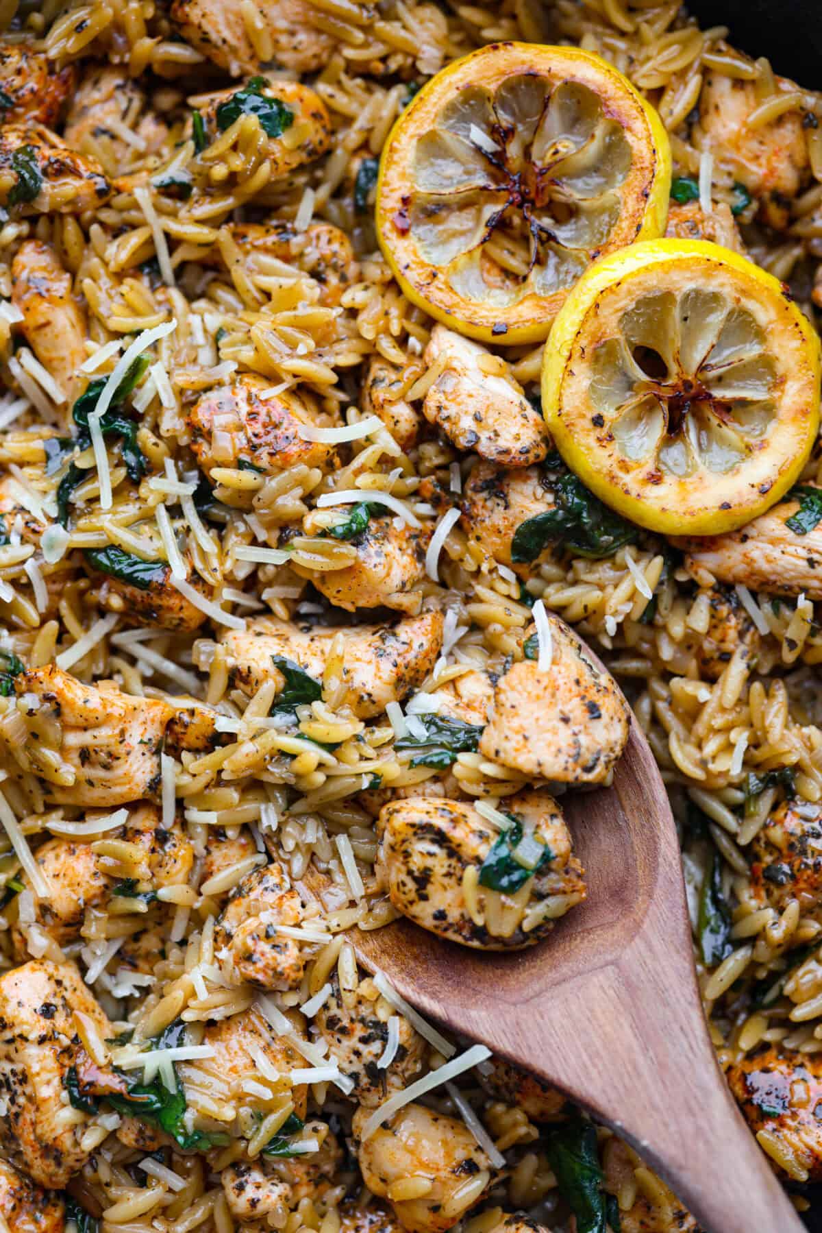 One-Pan Lemon Chicken Orzo is a comforting, well-rounded meal! Tender, juicy chicken pieces are joined with orzo pasta in a bright lemon sauce, resulting in melt-in-your-mouth deliciousness! Your whole family will adore this tasty dinner! Close up shot of chicken lemon orzo with wooden spoon.