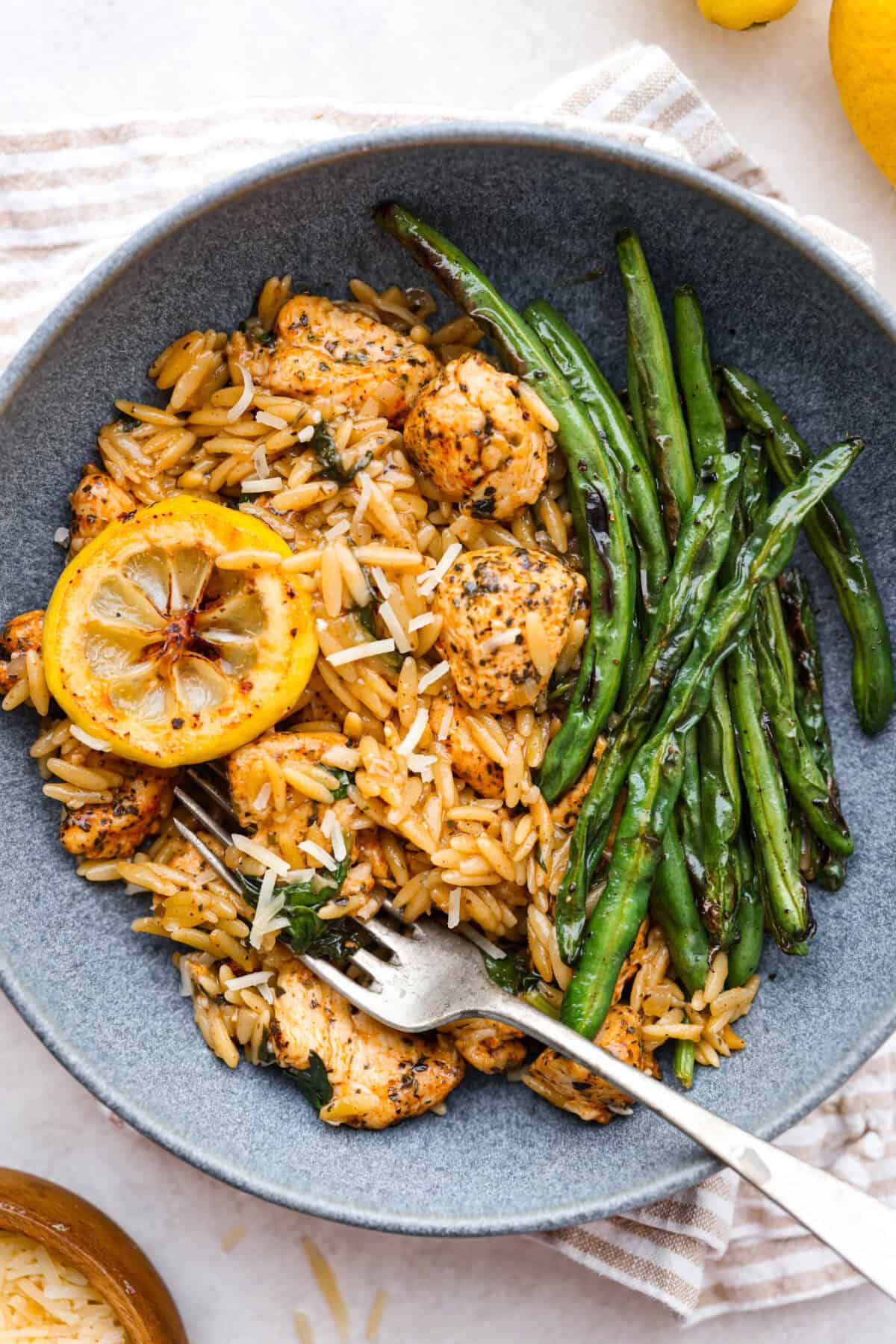 One-Pan Lemon Chicken Orzo is a comforting, well-rounded meal! Tender, juicy chicken pieces are joined with orzo pasta in a bright lemon sauce, resulting in melt-in-your-mouth deliciousness! Your whole family will adore this tasty dinner! Overhead shot of plated dish garnished with lemon slice and a side of green beans.