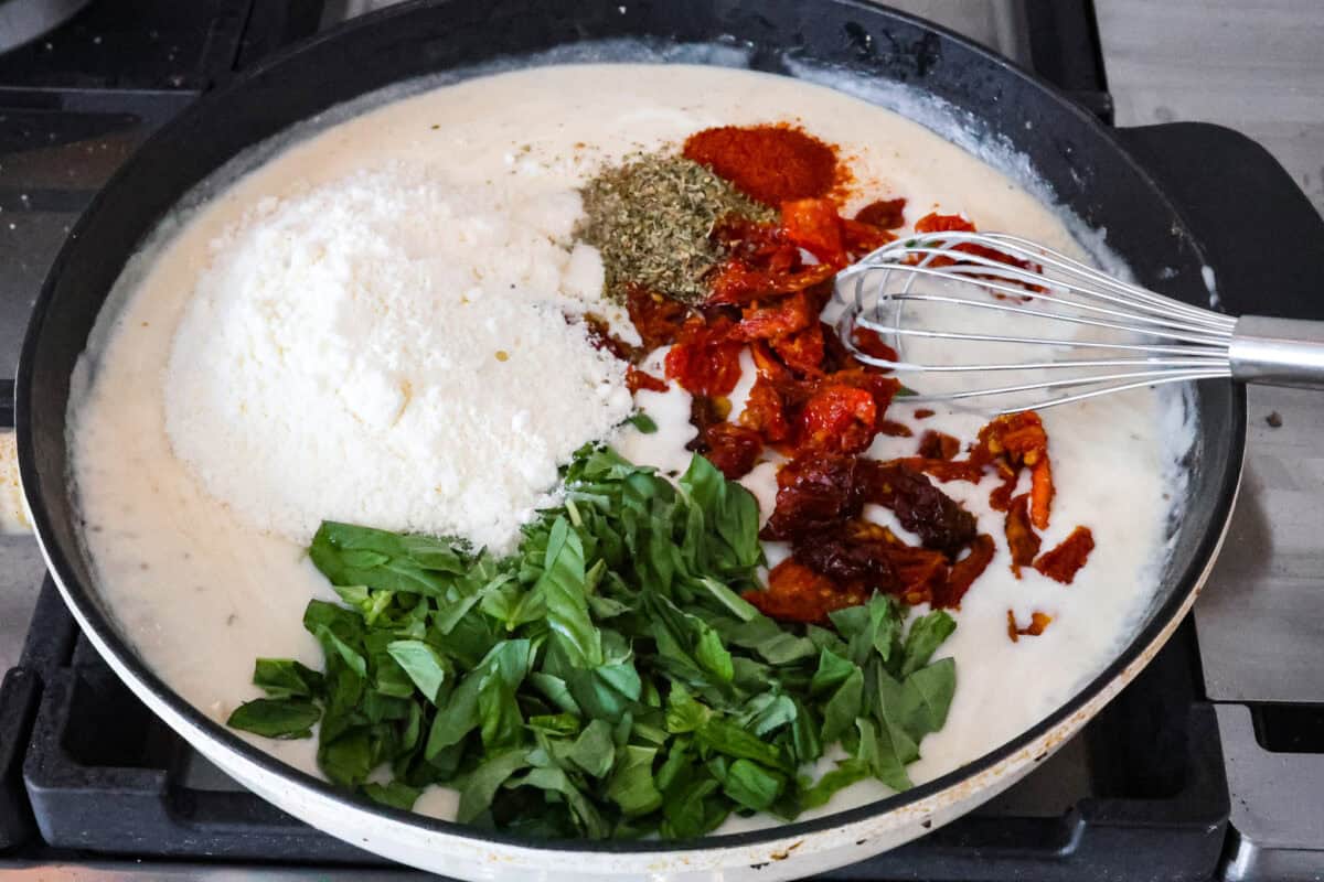 Marry Me Shrimp Pasta dazzles with robust Italian flavors. It's ready in just 30 minutes, and the creamy sauce, brimming with fresh herbs and spices, could very well lead to a marriage proposal after your first bite! Angle shot of skillet with sauce, basil, sun-dried tomatoes, parmesan and seasonings.