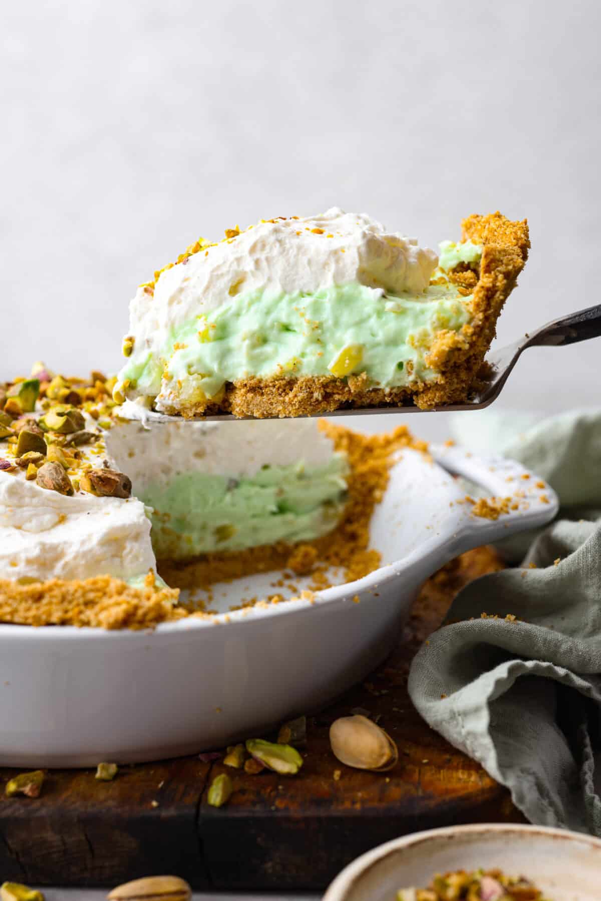 Bring this easy and irresistible no-bake pistachio cream pie to your next gathering! You'll love the combination of the pistachio and pineapple flavors that fill the inside of a sweet, buttery, graham cracker crust. Close side view of a slice of pie lifting from the pie dish.