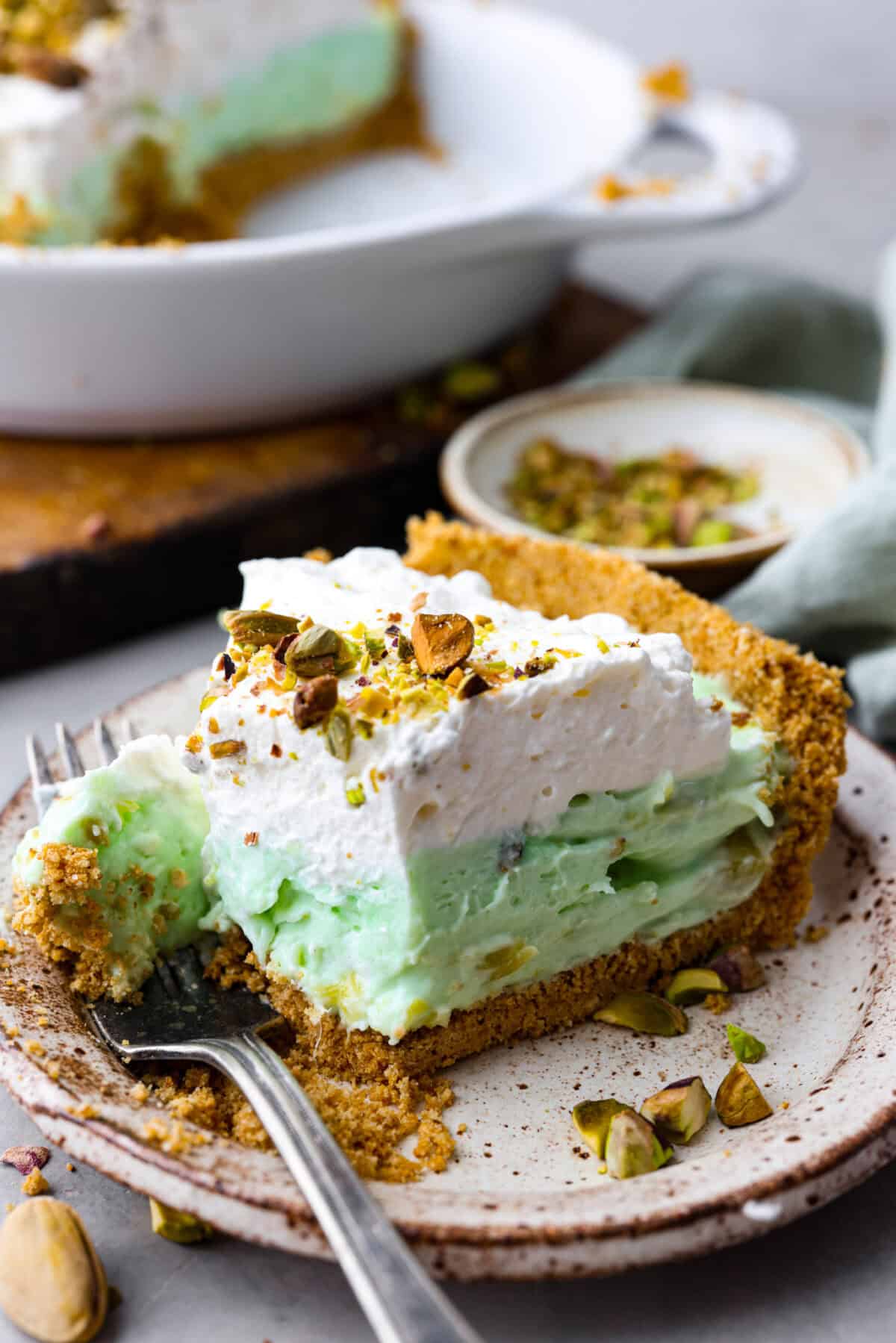 Bring this easy and irresistible no-bake pistachio cream pie to your next gathering! You'll love the combination of the pistachio and pineapple flavors that fill the inside of a sweet, buttery, graham cracker crust. Close view of a slice of pie on a plate.