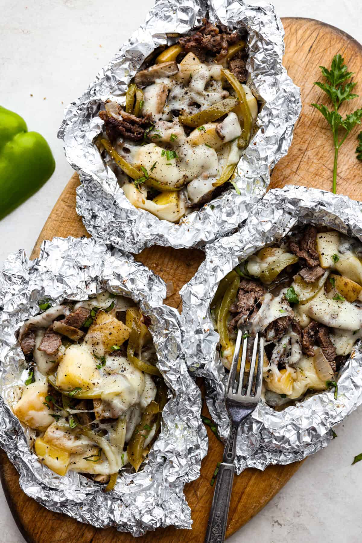 For a delicious chicken version, substitute the steak with thinly sliced chicken breasts or tenders. Adjust the cooking time accordingly for perfect tenderness. Overhead shot of 3 individual Philly cheesesteak foil packs open on a wood cutting board.