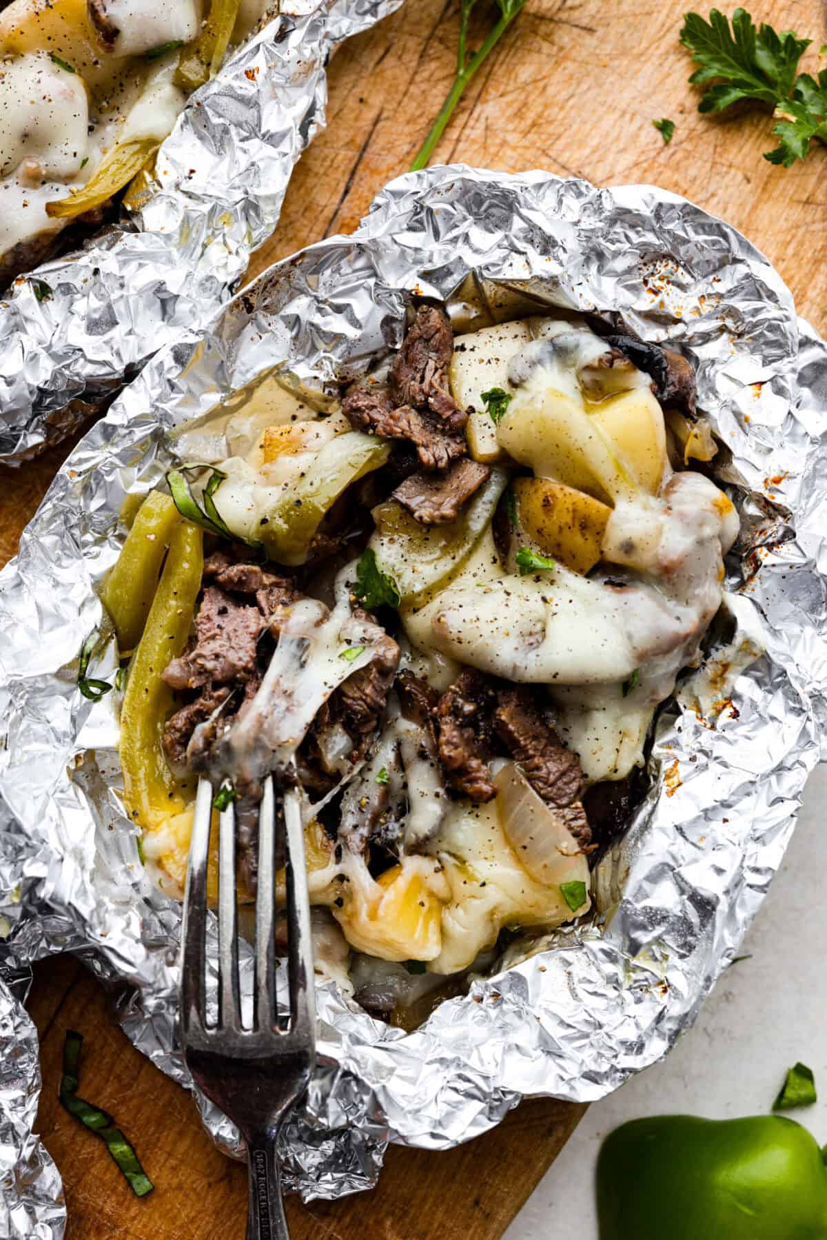 Try these delicious Philly Cheesesteak Foil Packs, a fun new way to enjoy the flavors of the classic Philly Cheesesteak. Tender beef, veggies, and melty cheese are grilled or baked together for a wonderful crowd-pleasing meal everyone will love! Over head shot of philly cheesesteak foil pack with fork.