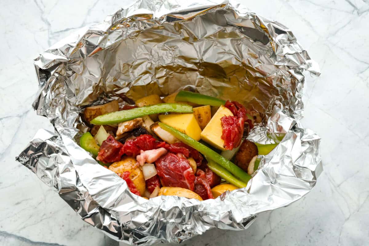 Try these delicious Philly Cheesesteak Foil Packs, a fun new way to enjoy the flavors of the classic Philly Cheesesteak. Tender beef, veggies, and melty cheese are grilled or baked together for a wonderful crowd-pleasing meal everyone will love! Overhead shot of foil with raw meat and veggie mixture in it.