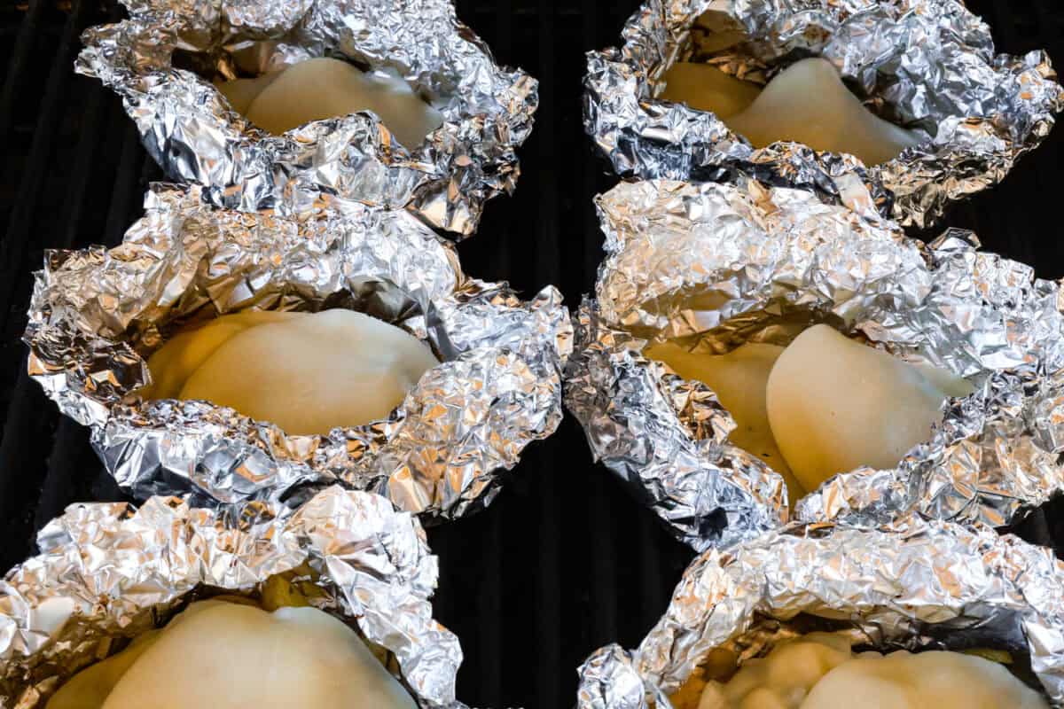 Try these delicious Philly Cheesesteak Foil Packs, a fun new way to enjoy the flavors of the classic Philly Cheesesteak. Tender beef, veggies, and melty cheese are grilled or baked together for a wonderful crowd-pleasing meal everyone will love! Angle shot of foil packs open on the grill with cheese on top of the veggie and meat mixture.
