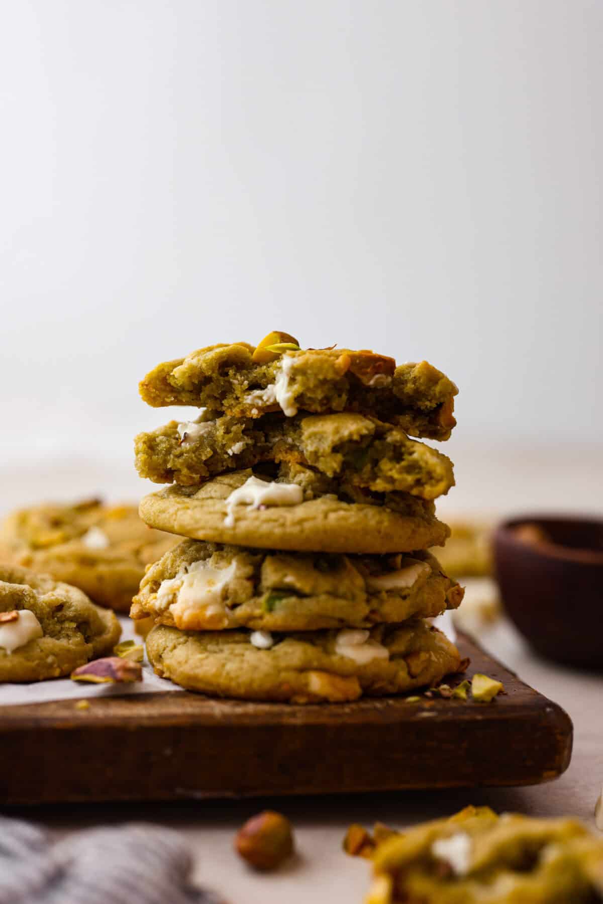 Pistachio Pudding Cookies are super soft, chewy, and irresistible! They're easy to make, and adding pistachio pudding mix gives this cookie recipe wonderful flavor and the perfect tender texture! Side shot of stacked pistachio pudding cookies on a wood cutting board.