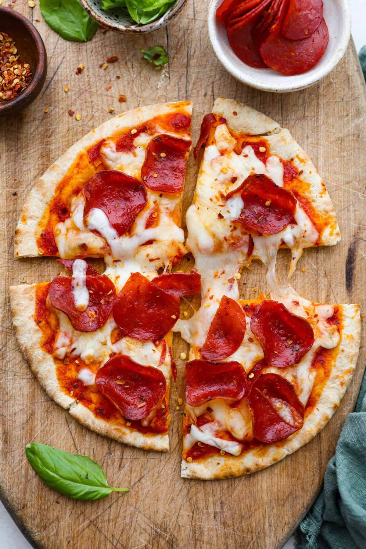Pita pizza is like having your own personalized mini-pizza! Grab some ready-made pitas, pile on your favorite toppings, and indulge in a quick and tasty snack for a delightful way to satisfy your pizza craving whenever it strikes! Overhead shot of sliced pita pizza on cutting board.
