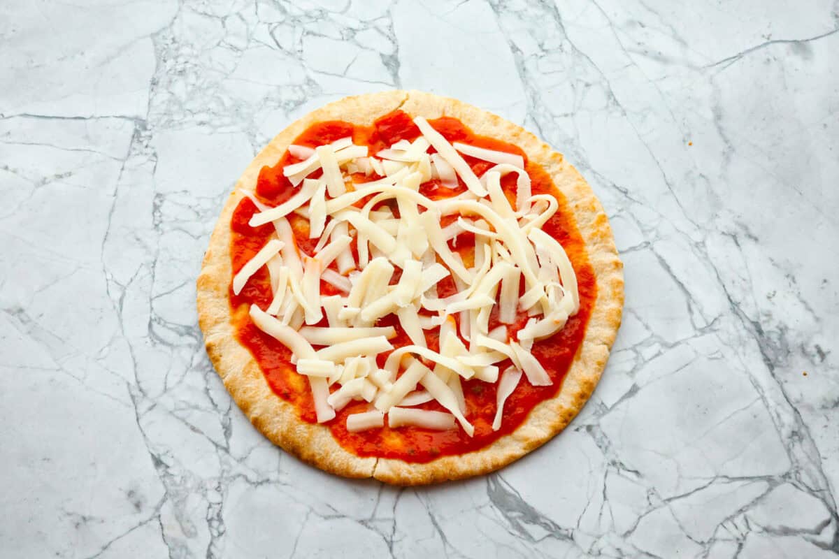 Pita pizza is like having your own personalized mini-pizza! Grab some ready-made pitas, pile on your favorite toppings, and indulge in a quick and tasty snack for a delightful way to satisfy your pizza craving whenever it strikes! Overhead shot of pita with marinara and cheese spread on top.