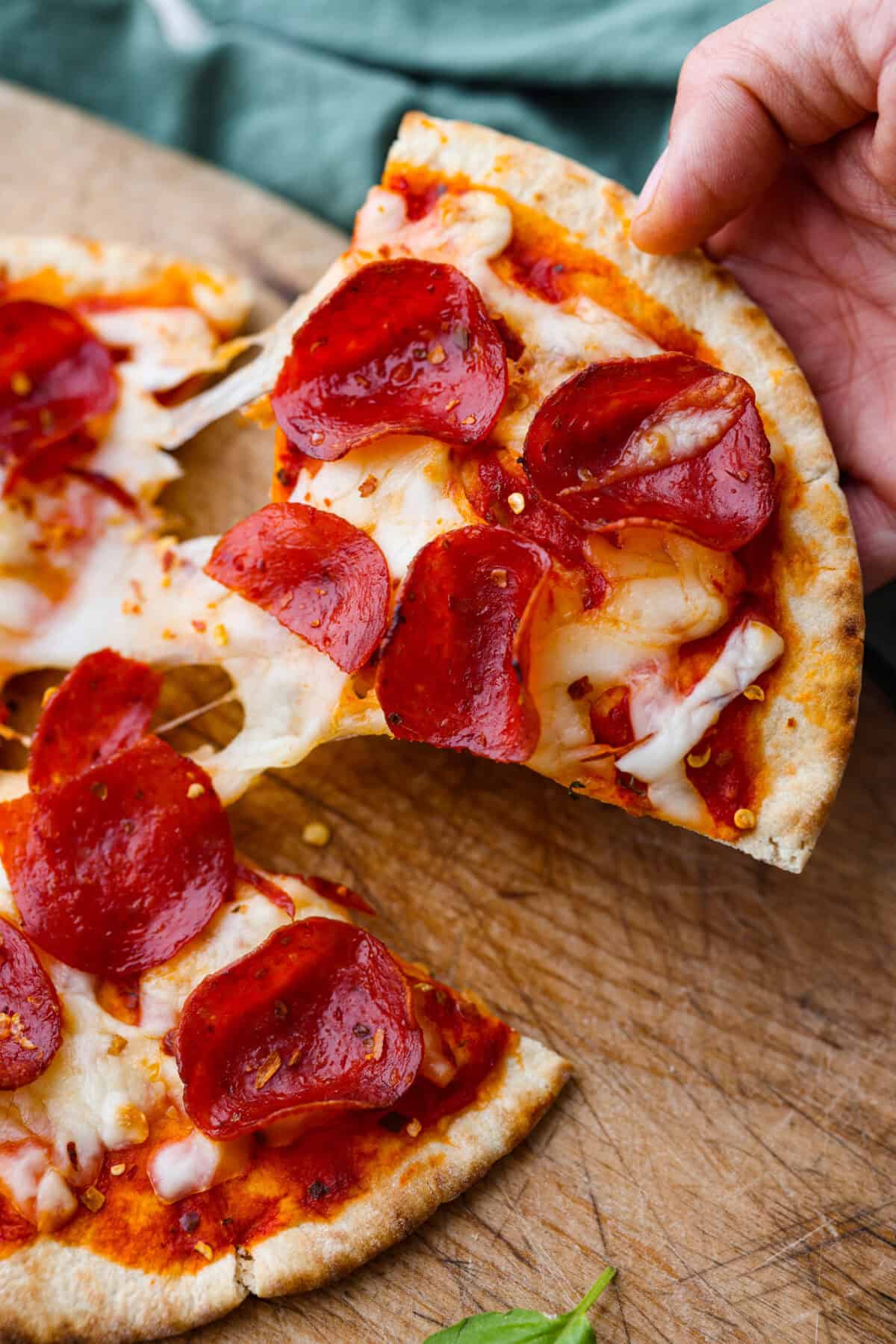 Pita pizza is like having your own personalized mini-pizza! Grab some ready-made pitas, pile on your favorite toppings, and indulge in a quick and tasty snack for a delightful way to satisfy your pizza craving whenever it strikes! Angle shot of someone picking up a slice of pita pizza.