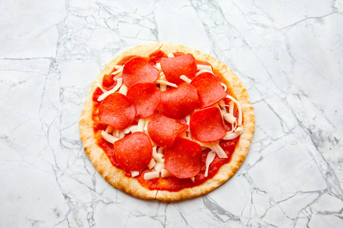 Pita pizza is like having your own personalized mini-pizza! Grab some ready-made pitas, pile on your favorite toppings, and indulge in a quick and tasty snack for a delightful way to satisfy your pizza craving whenever it strikes! Overhead shot of pita with marinara, cheese and pepperoni.