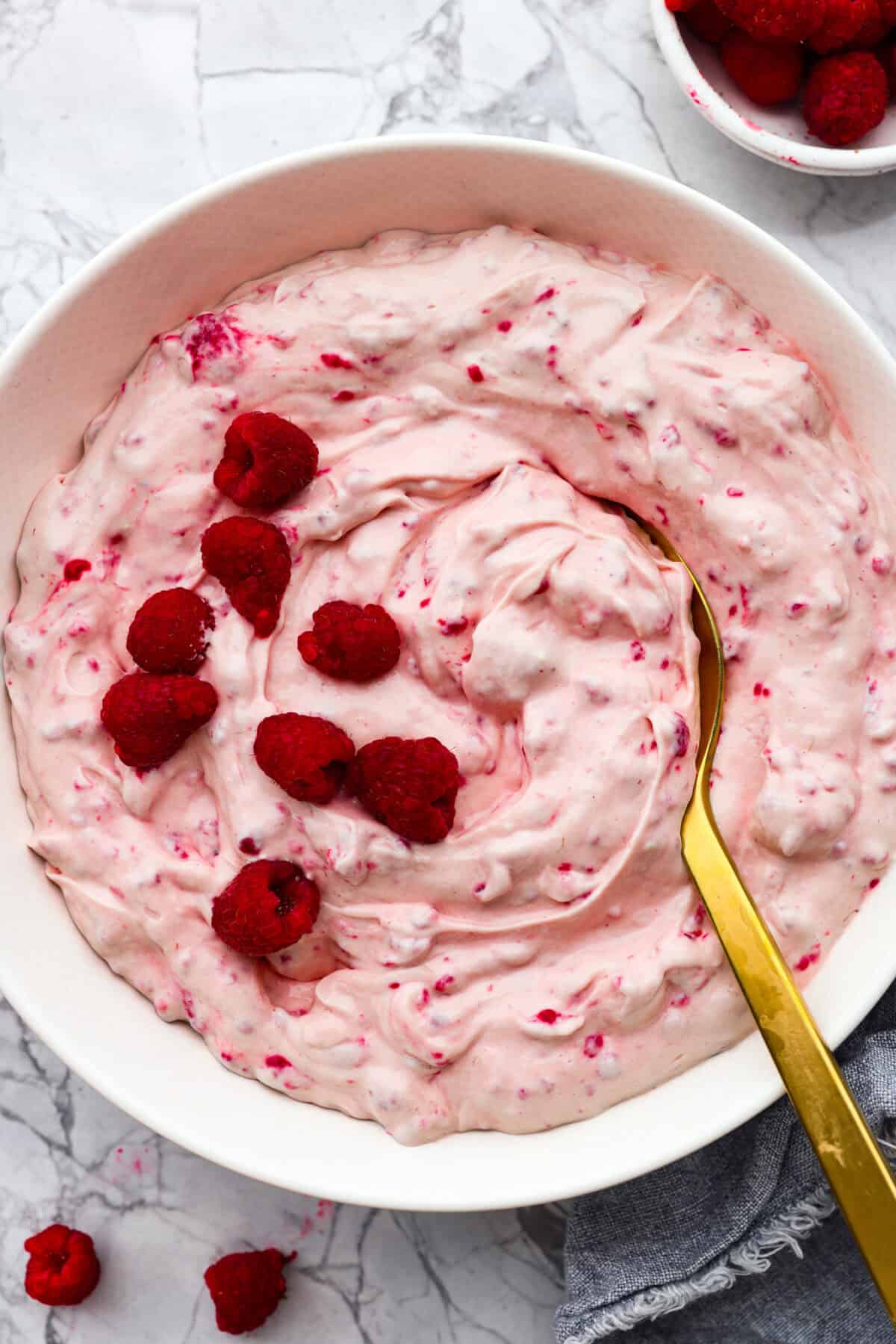 Fresh and fruity Raspberry Fluff Salad is a sweet and creamy side or dessert with a mix of raspberries, vanilla yogurt and Cool Whip. Made with just 4 ingredients in 5 minutes, it's SO easy to make and perfect for potlucks and picnics! The top view of a raspberry fluff salad.