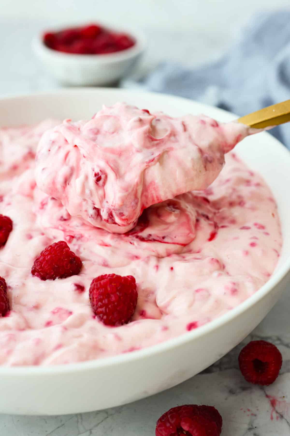 Fresh and fruity Raspberry Fluff Salad is a sweet and creamy side or dessert with a mix of raspberries, vanilla yogurt and Cool Whip. Made with just 4 ingredients in 5 minutes, it's SO easy to make and perfect for potlucks and picnics! A close up side view of a scoop of raspberry fluff salad with a gold spoon.