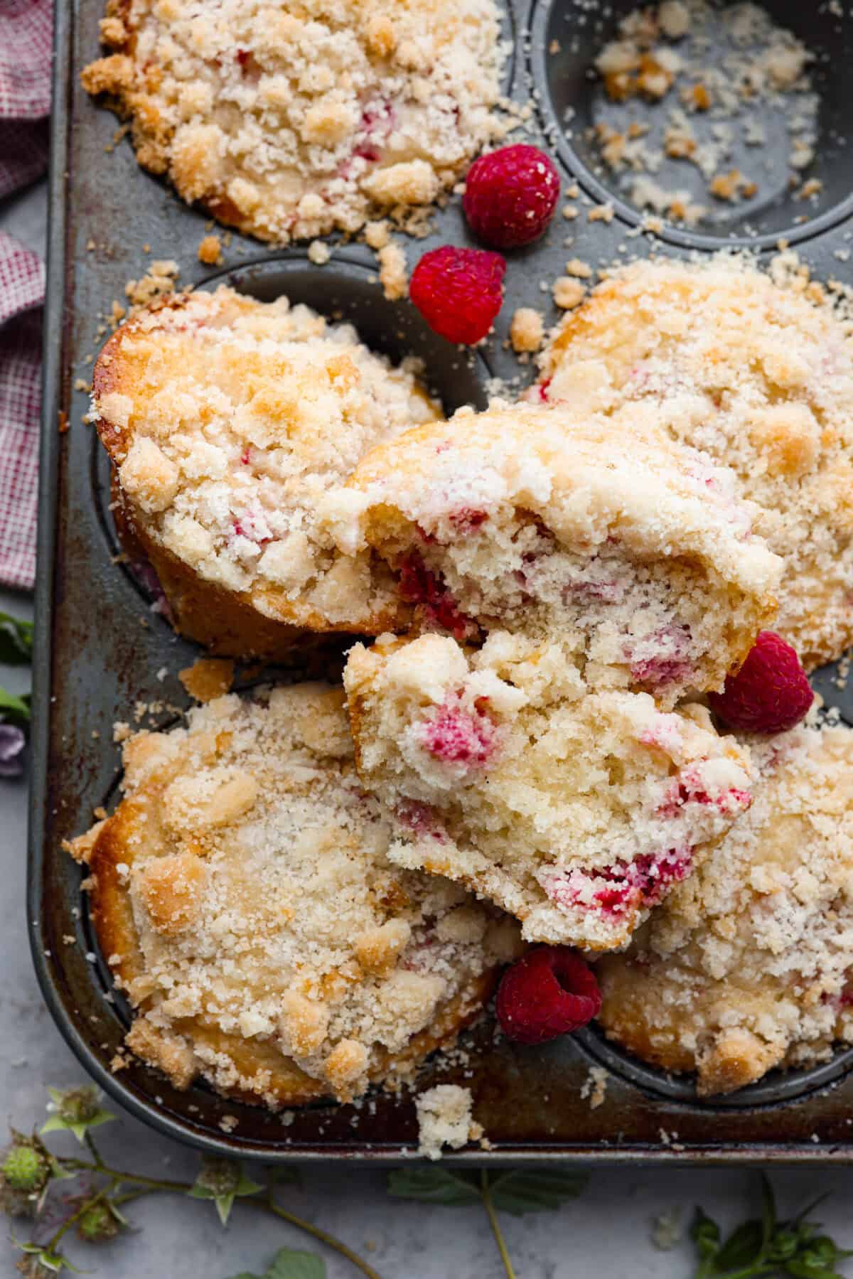 These raspberry muffins are moist and delicious, filled with plump fresh raspberries and topped with a sweet, crunchy streusel topping! They are perfect for a warm breakfast, brunch, or as an after-school or work snack. Your family will be begging for more, so donโt expect them to last long! Close up shot of raspberry muffins broken up on top of muffin tin.