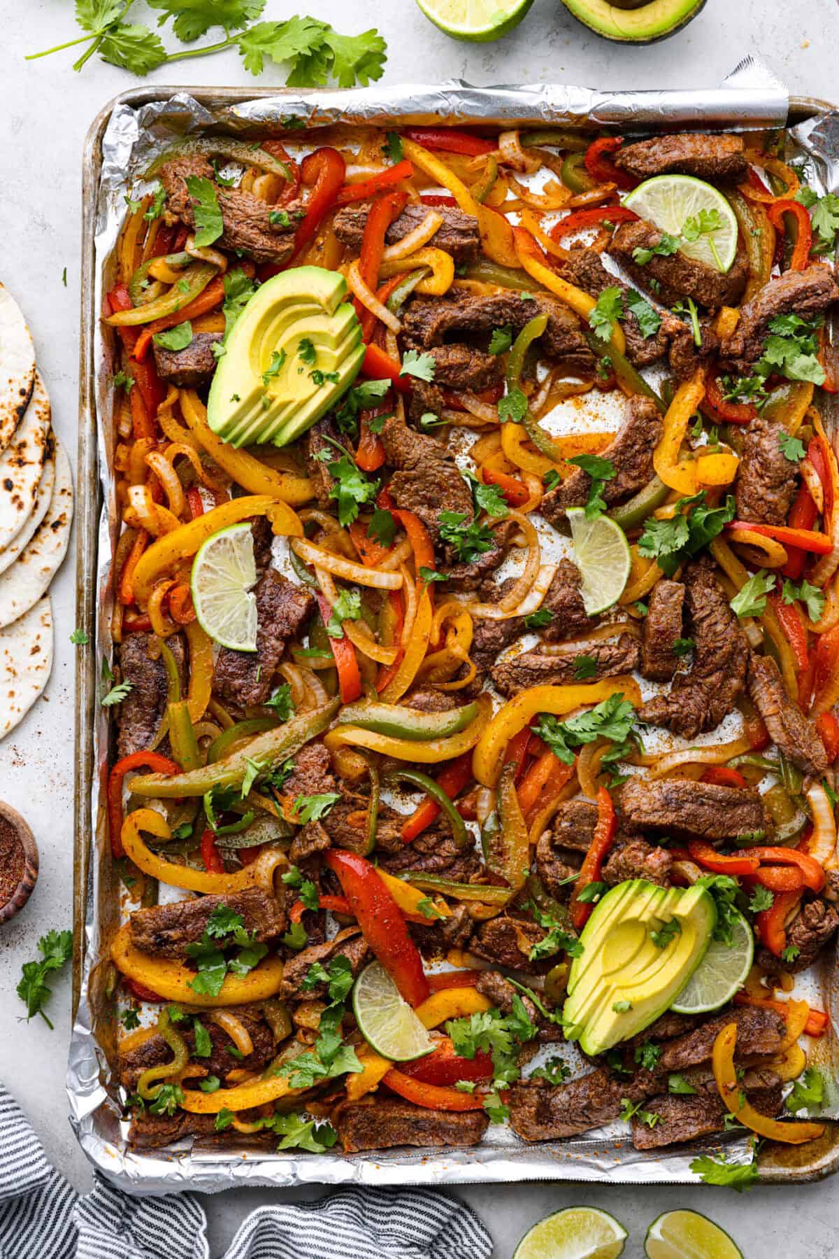 Sheet pan steak fajitas are beautiful and bursting with flavor. Easy to throw together on busy weeknights, they feature tender steak and crisp, colorful vegetables in every bite. You will definitely want to add this to your weekly meal planning! Overhead shot of cooked sheet pan steak fajitas.