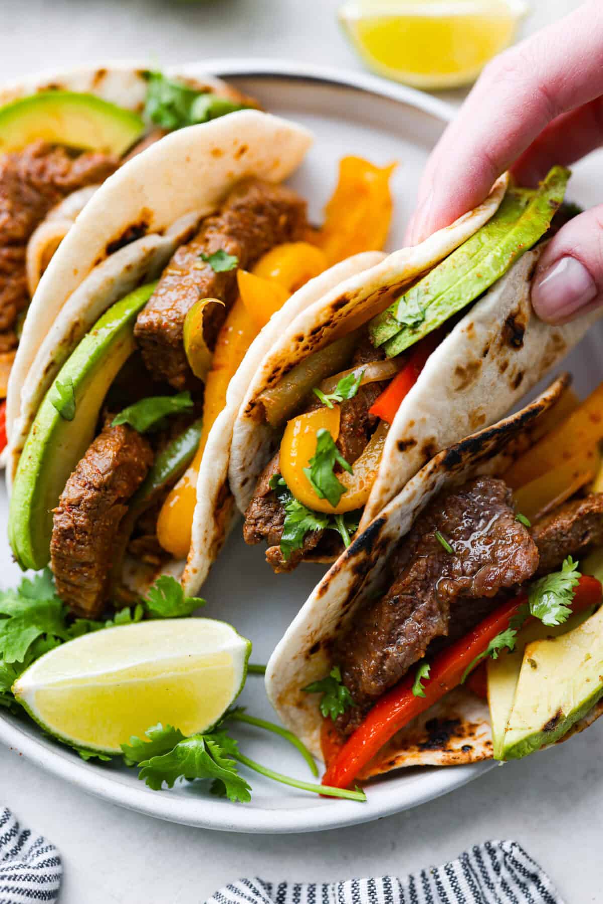 Sheet pan steak fajitas are beautiful and bursting with flavor. Easy to throw together on busy weeknights, they feature tender steak and crisp, colorful vegetables in every bite. You will definitely want to add this to your weekly meal planning! Angel shot of someone picking up a tortilla filled with fajita mix and topped with avocado.