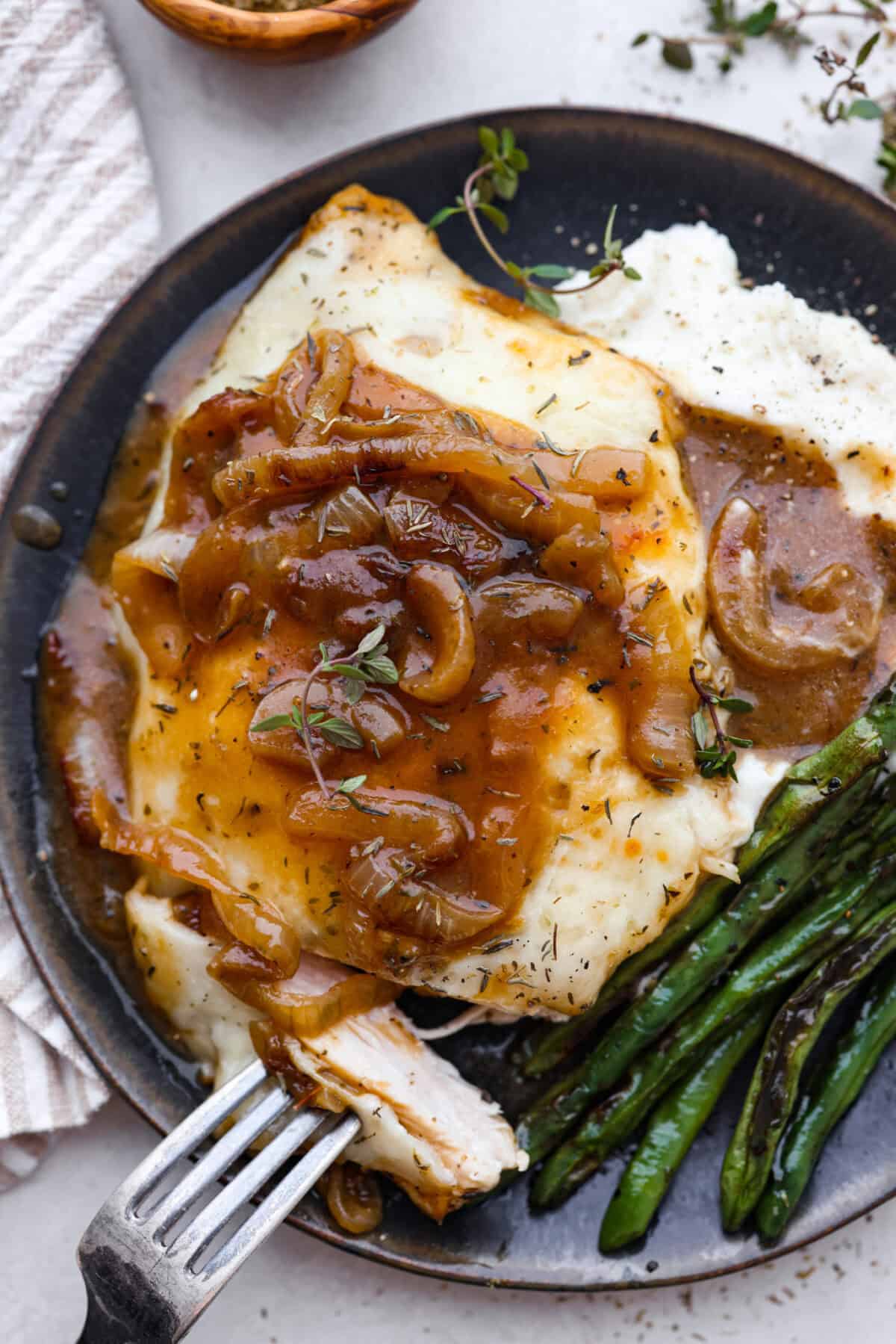 Skillet French Onion Chicken delivers a tender and creamy chicken dinner that you can make at home, it's easily better than anything you can find in a restaurant. Your family will love this incredibly delicious meal, making it an instant favorite! Overhead shot of plated chicken on potatoes with a bite on a fork.