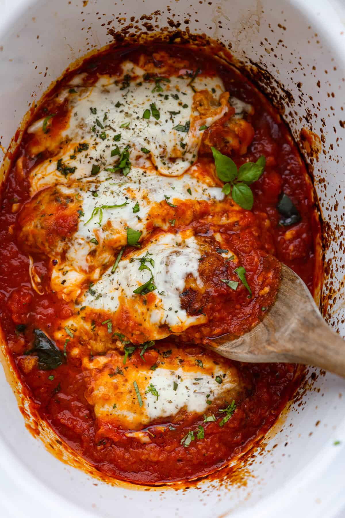 This simple slow-cooker chicken parmesan is full of delicious Italian flavors, oozy cheese, and mouthwatering marinara sauce. You'll be able to throw everything in the crock pot, set it, and forget it—dinner is served! Overhead shot of cooked slow cooker chicken parmesan.