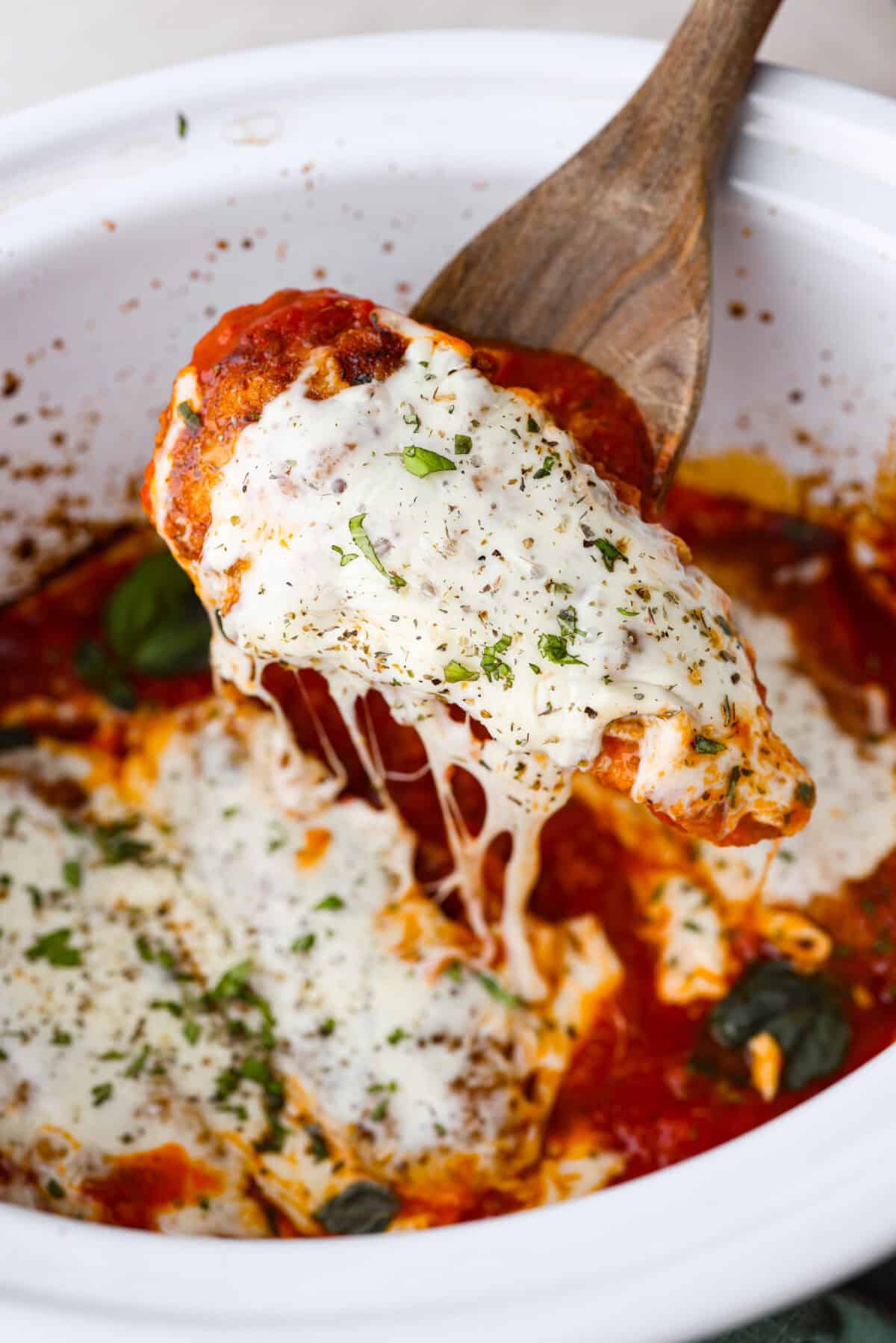 This simple slow-cooker chicken parmesan is full of delicious Italian flavors, oozy cheese, and mouthwatering marinara sauce. You'll be able to throw everything in the crock pot, set it, and forget it—dinner is served! Angle shot of someone lifting a slow cooker chicken parmesan chicken tender out of the crock pot.