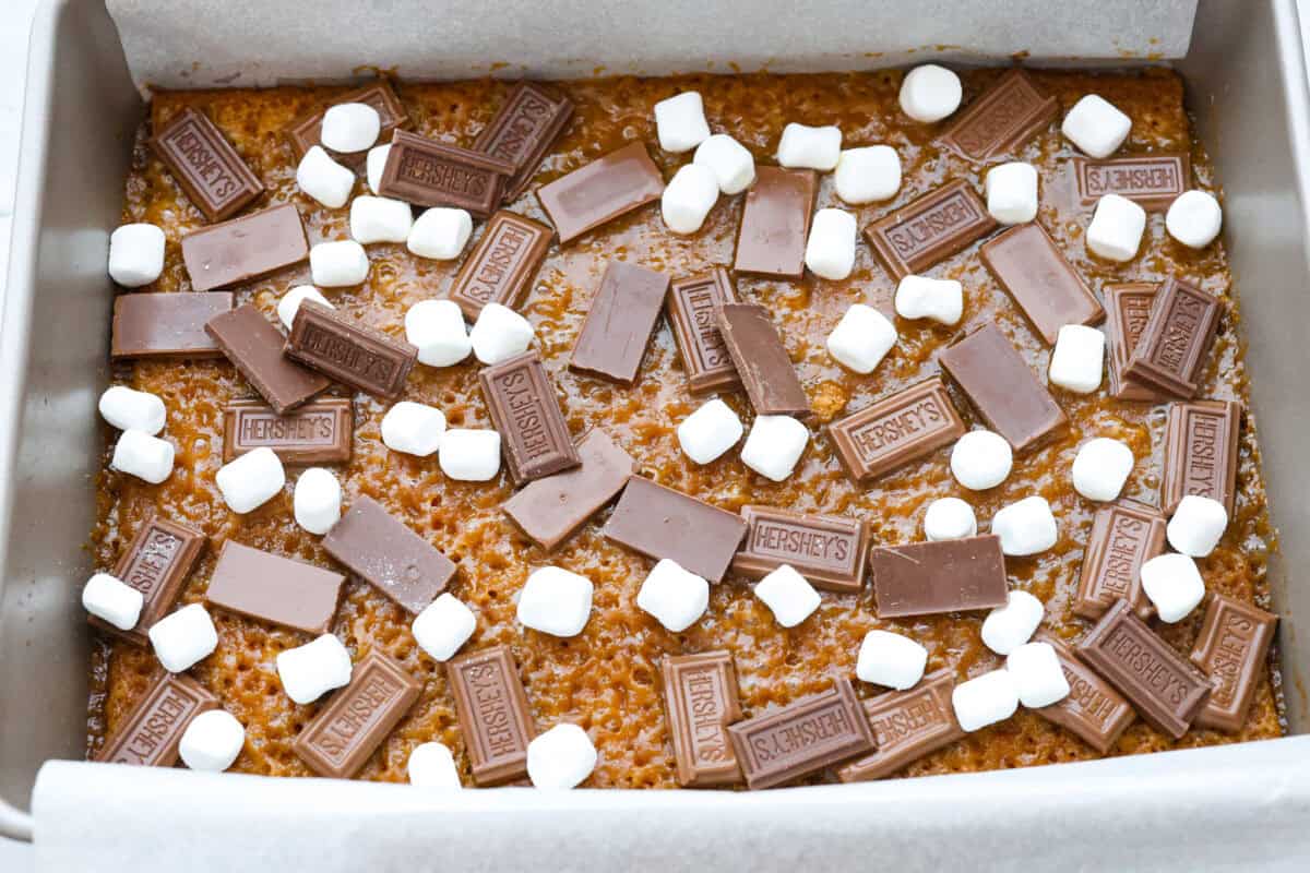 S'mores crack is a quick way to enjoy the classic s'more experience without a campfire. Featuring a buttery graham cracker crust, rich melted chocolate, and toasted marshmallows, this treat will quickly become a family favorite. Overhead shot of of the pan with graham cracker layer with butter and sugar mixture topped with pieces of chocolate and mini marshmallows.