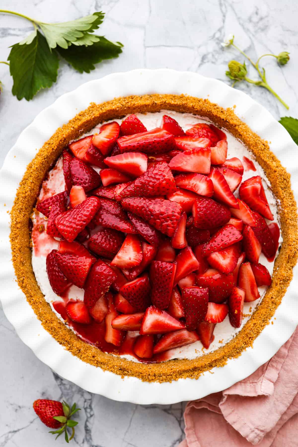 This strawberry cream cheese pie has a smooth, creamy filling is topped with sweet strawberries and is held together by a crumbly, buttery crust. Simply divine! Overhead view of strawberry cream cheese pie, in whit pie pan on marble countertop.