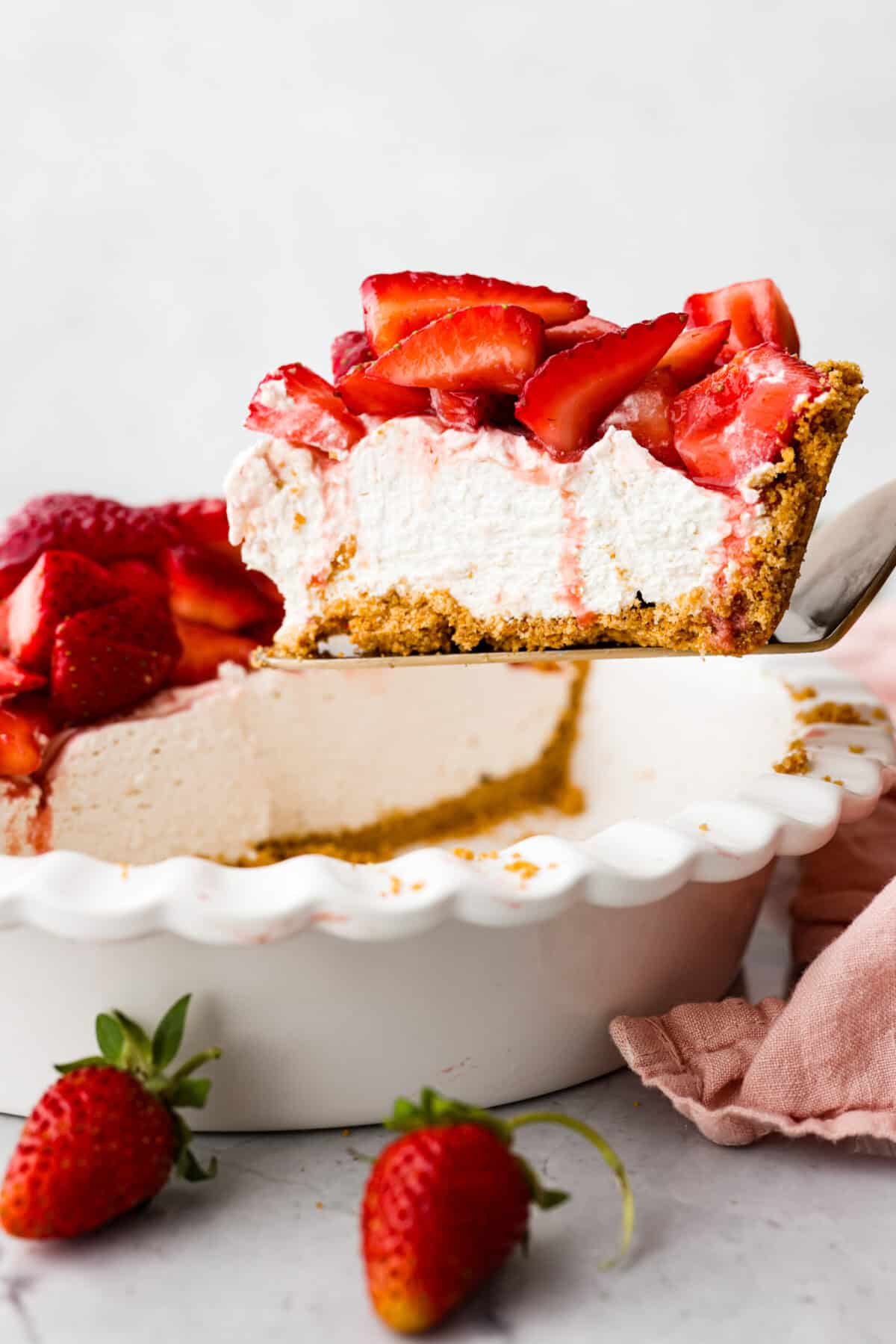 This strawberry cream cheese pie has a smooth, creamy filling is topped with sweet strawberries and is held together by a crumbly, buttery crust. Simply divine! Side view of slice of pie being lifted out of pie dish