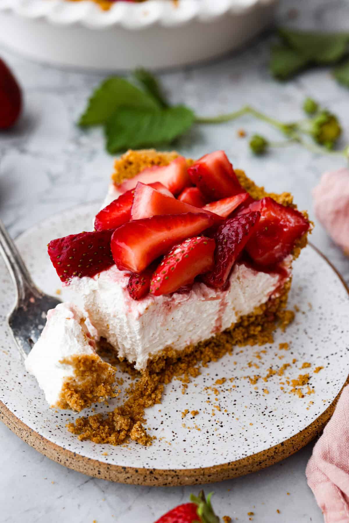 This strawberry cream cheese pie has a smooth, creamy filling is topped with sweet strawberries and is held together by a crumbly, buttery crust. Simply divine! Angle shot of a slice of strawberry cream pie on a plate with a bite taken out on a fork next to it.