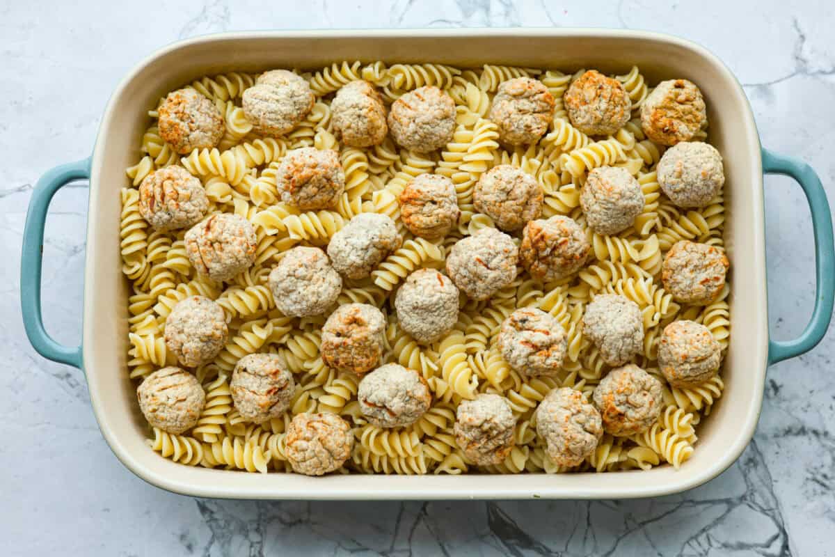 Swedish Meatball Casserole is a classic comfort meal the whole family will enjoy! Tender meatballs are layered over perfectly cooked pasta and baked in a rich, creamy gravy. This dinner recipe is easy enough to make during the week but also deliciously impressive for entertaining! Overhead shot of casserole dish with pasta on the bottom with meatballs spaced out on top.