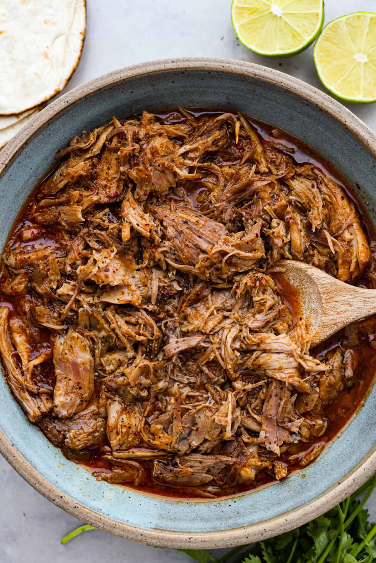 This is the BEST sweet pork taco recipe! It tastes just like Cafe Rio's famous sweet pork, with a blend of sweet and tangy flavors that melt into tender, juicy meat. It's perfect for tacos, salads, burritos, nachos, and anything else you can dream up! Sweet pork in large serving bowl with wooden spoon.