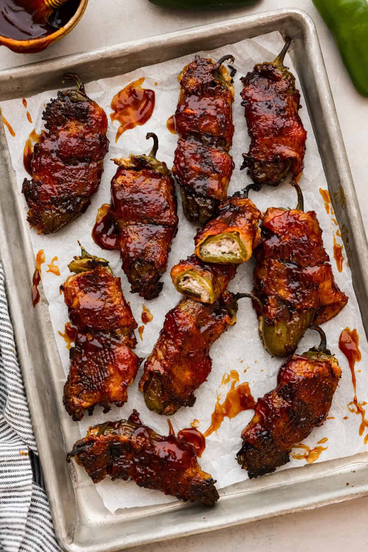 Texas Twinkies are a major upgrade to your classic jalapeรฑo poppers! They're jalapeรฑos filled with cream cheese, brisket, and shredded cheese, then wrapped in bacon and cooked to perfection. These are the hit of any party! Overhead shot of Texas Twinkies lined up on a sheet pan.