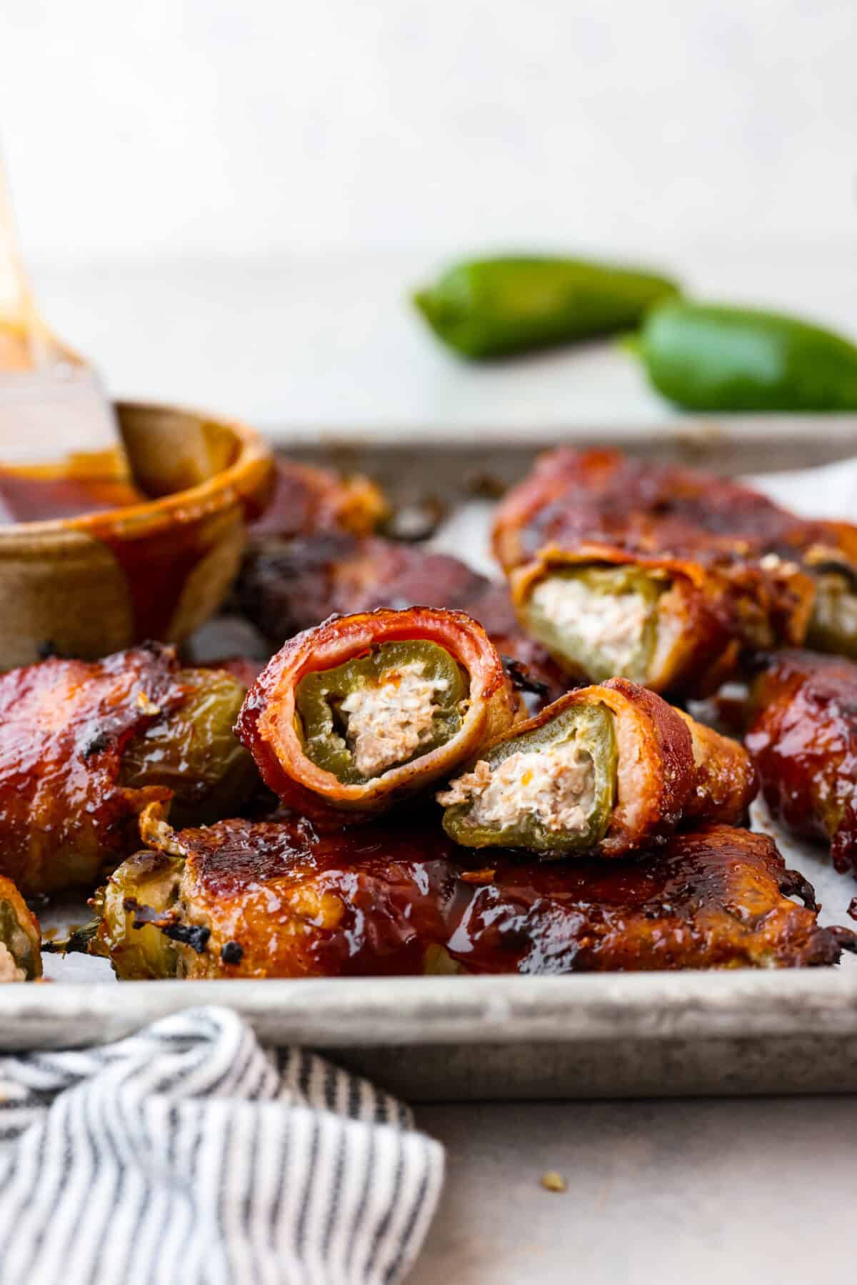 Texas Twinkies are a major upgrade to your classic jalapeรฑo poppers! They're jalapeรฑos filled with cream cheese, brisket, and shredded cheese, then wrapped in bacon and cooked to perfection. These are the hit of any party! Side shot of pan of Texas Twinkies with one on top cut in half to reveal the filling.