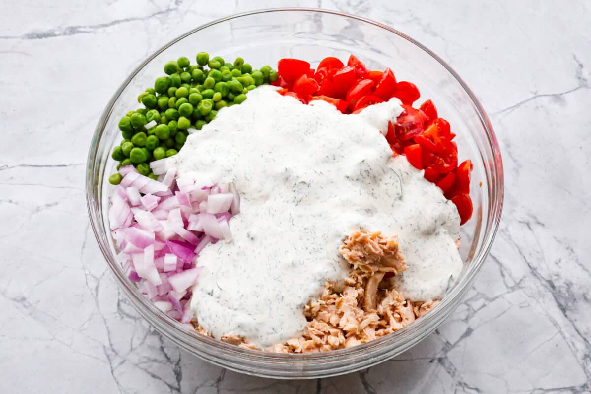 Tuna pasta salad is a perfect protein-packed lunch or side dish! It combines tuna, veggies, and pasta then gets tossed in a creamy dill dressing. Third photo of the dressing poured on top of the salad ingredients before tossing.