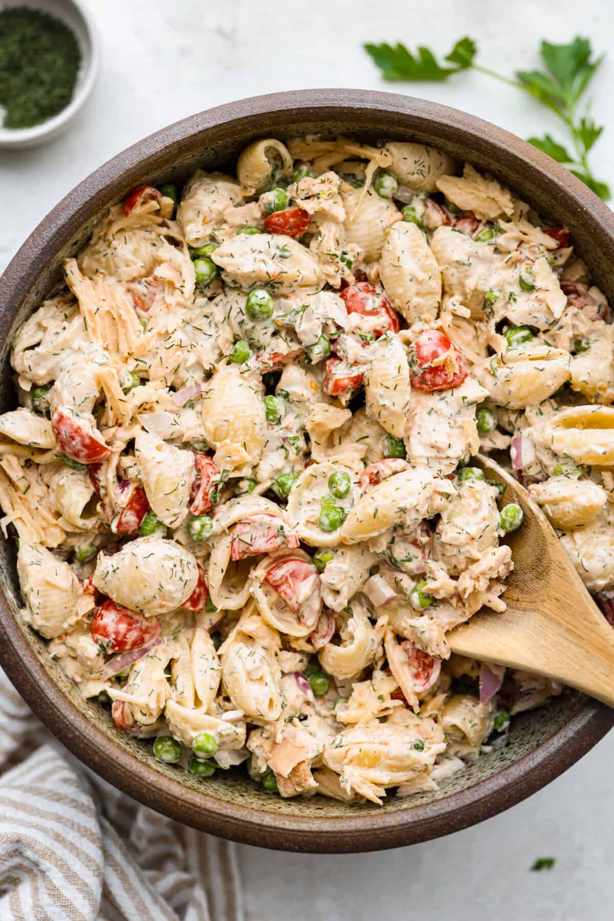Tuna pasta salad is a perfect protein-packed lunch or side dish! It combines tuna, veggies, and pasta then gets tossed in a creamy dill dressing. Top view of tuna pasta salad in a bowl with a wood spoon.