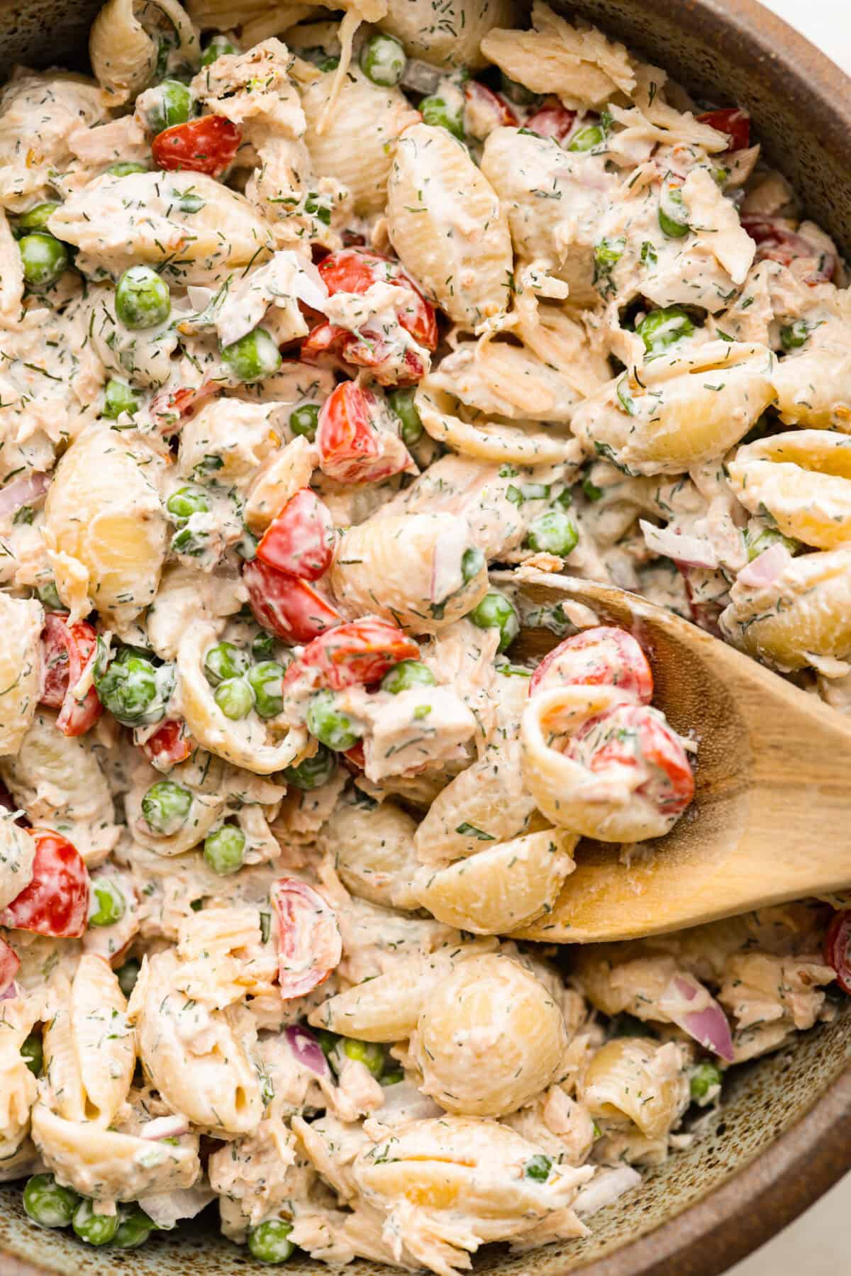 Tuna pasta salad is a perfect protein-packed lunch or side dish! It combines tuna, veggies, and pasta then gets tossed in a creamy dill dressing. Top close view of a wood spoon in the pasta salad.